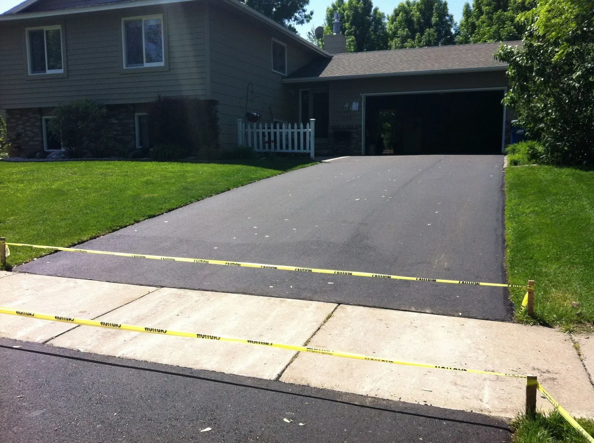 Newly paved asphalt driveway, sidewalk in front, house in background. Yellow tape blocks access.