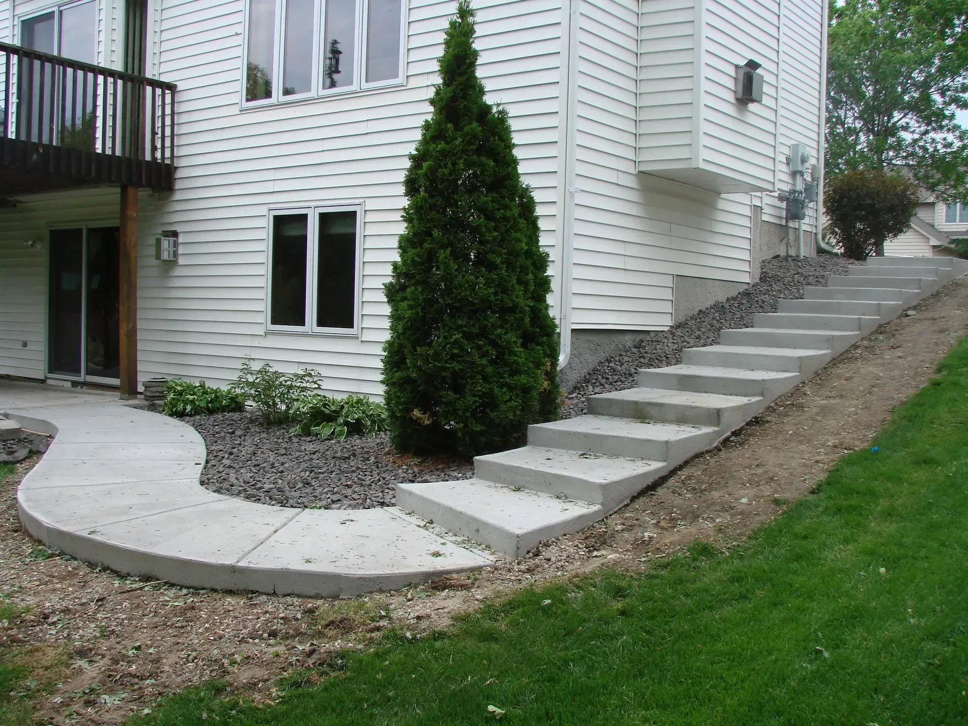 Concrete stairs and pathway leading up to a white building with a small evergreen tree and lawn.