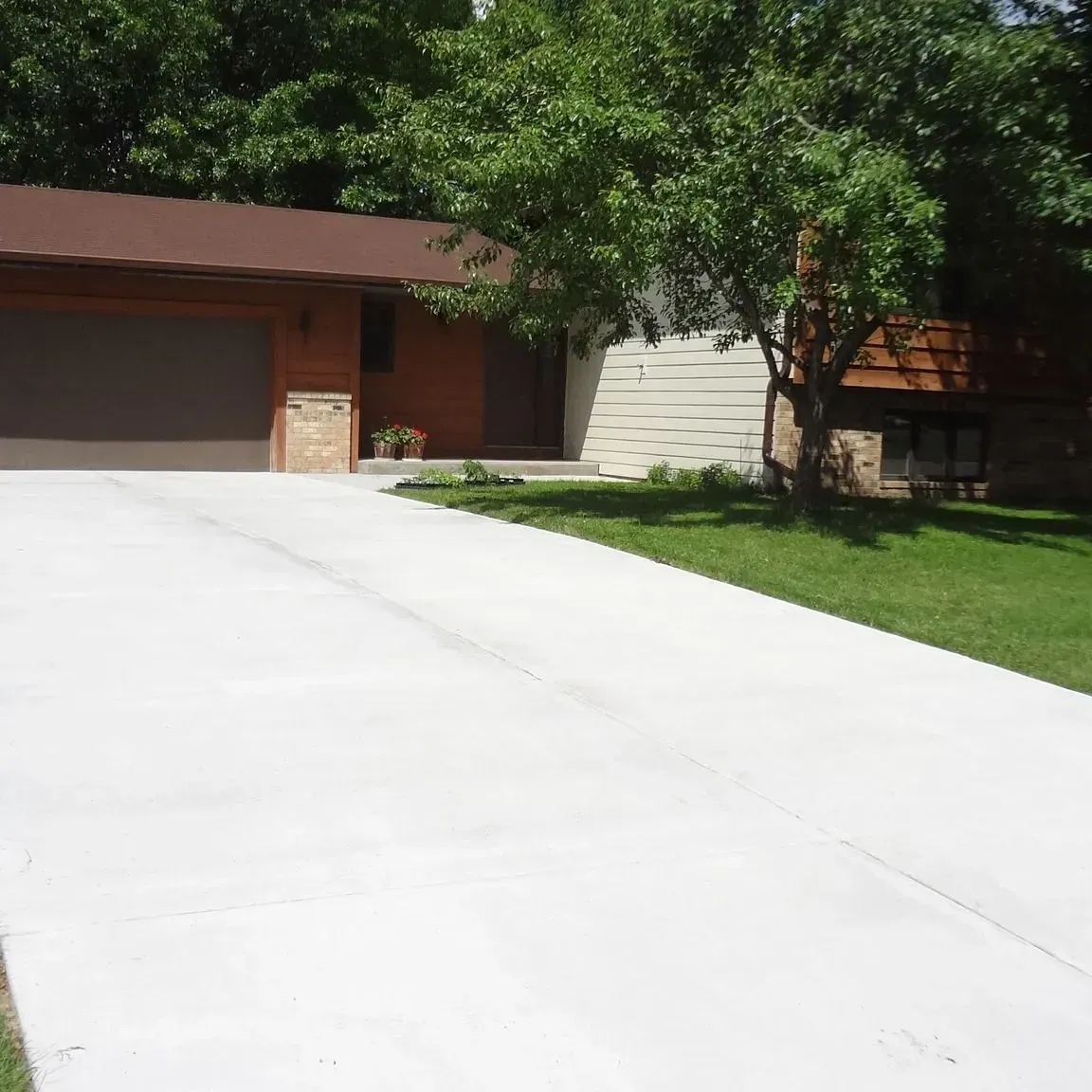 Concrete driveway leading to a brown house with a garage and lush green lawn.