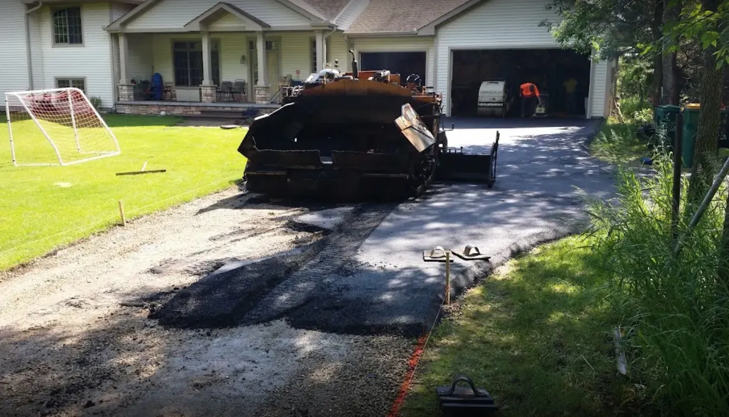 Asphalt paving machine resurfacing a residential driveway.