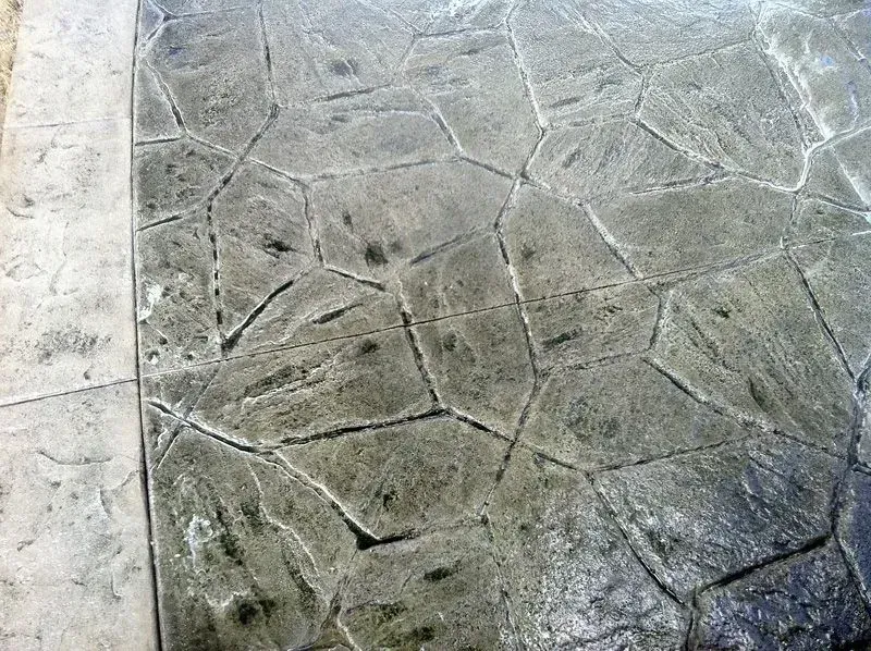 Curved, layered retaining wall with grass in foreground, trees and hillside in background.