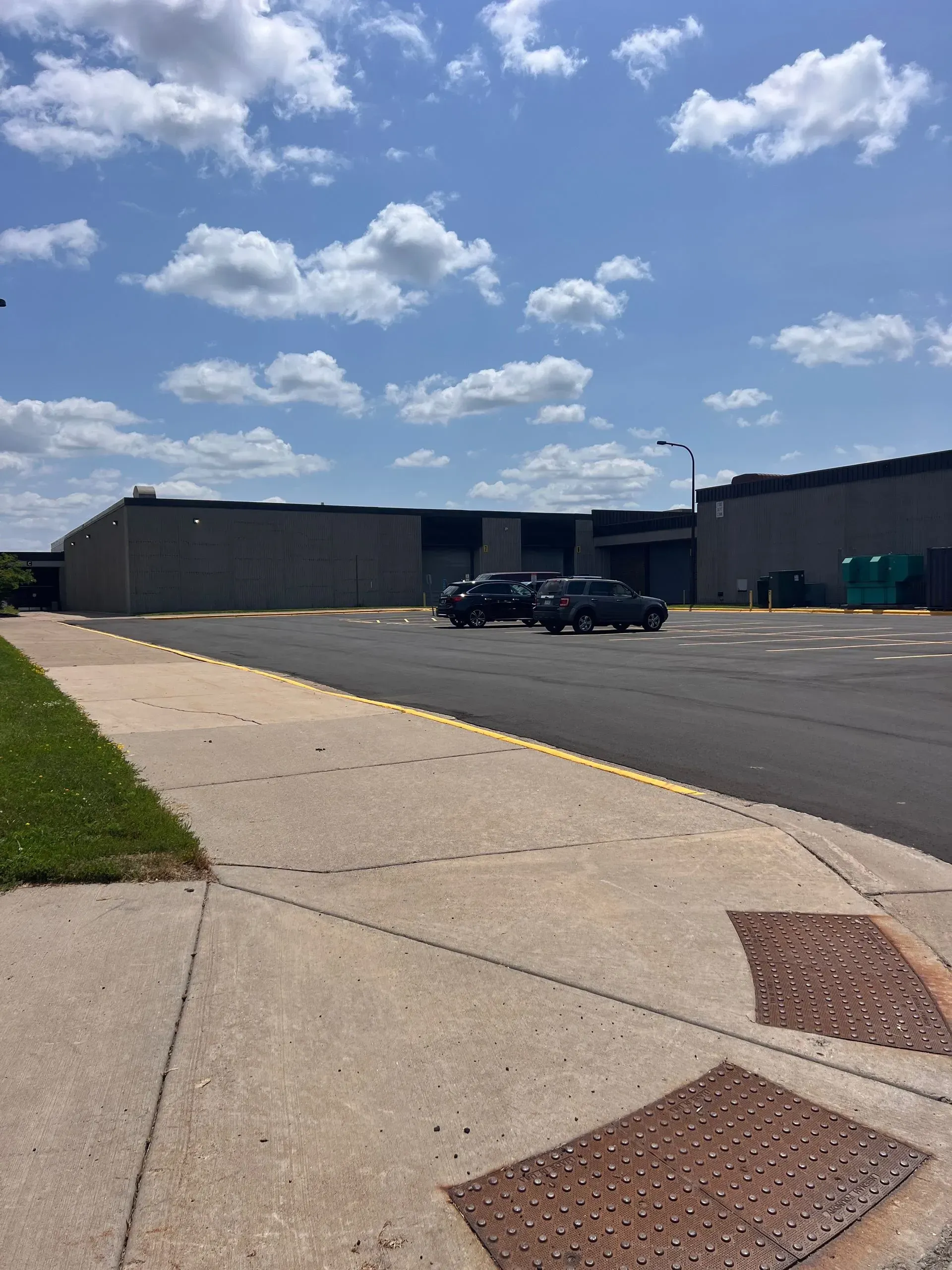 Exterior view of a building with cars parked in front, sidewalk, and a cloudy blue sky.