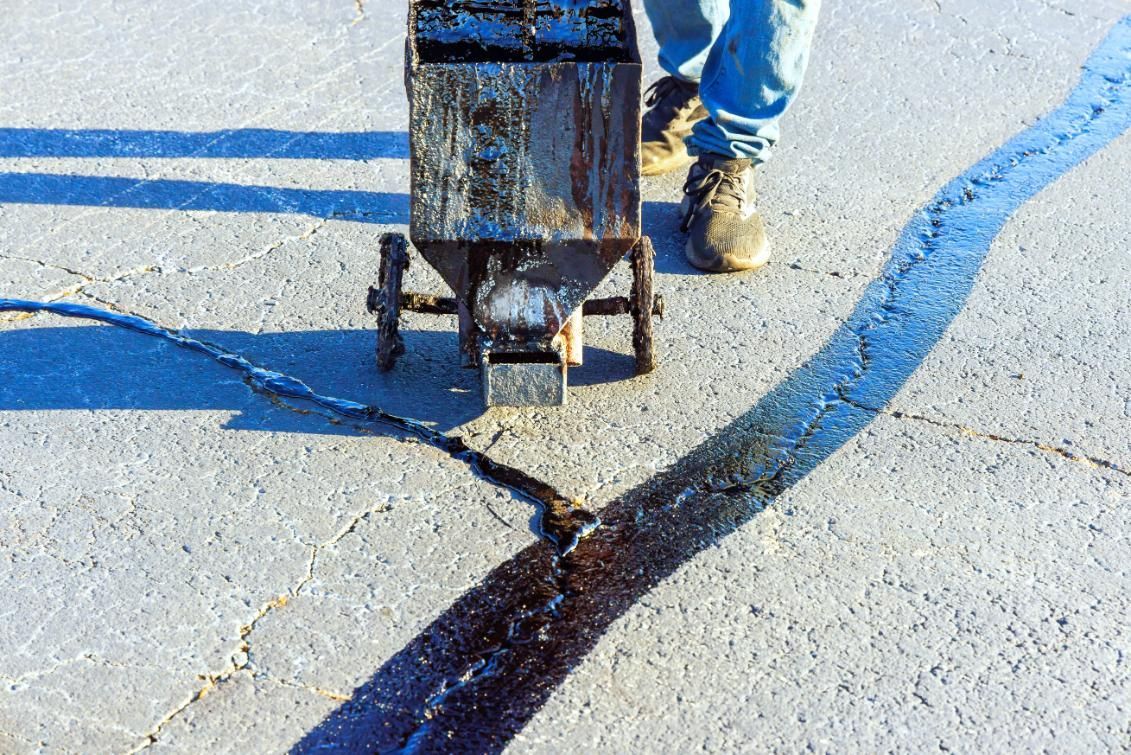 Person applying sealant to a crack in asphalt using a specialized machine.