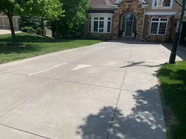 Concrete driveway leading to a stone-faced house with a basketball hoop. Lush green grass surrounds.