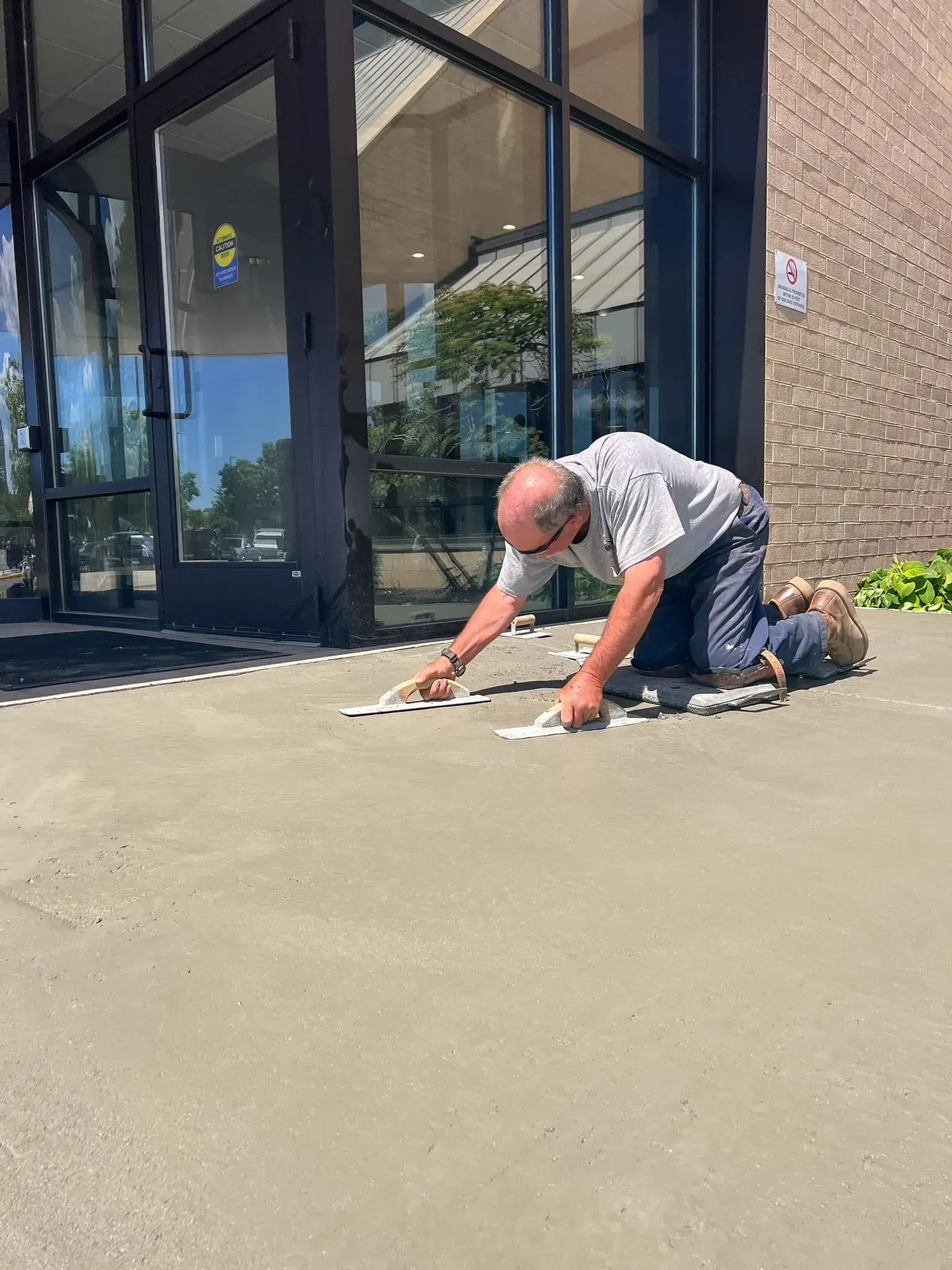 Man kneeling on concrete, placing small white papers near building entrance on a sunny day.