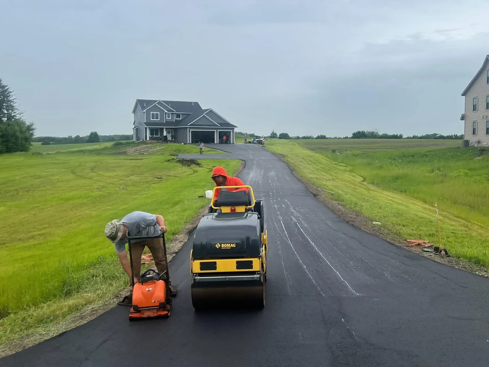 Two workers paving a driveway with roller and vibratory plate compactor; residential setting.