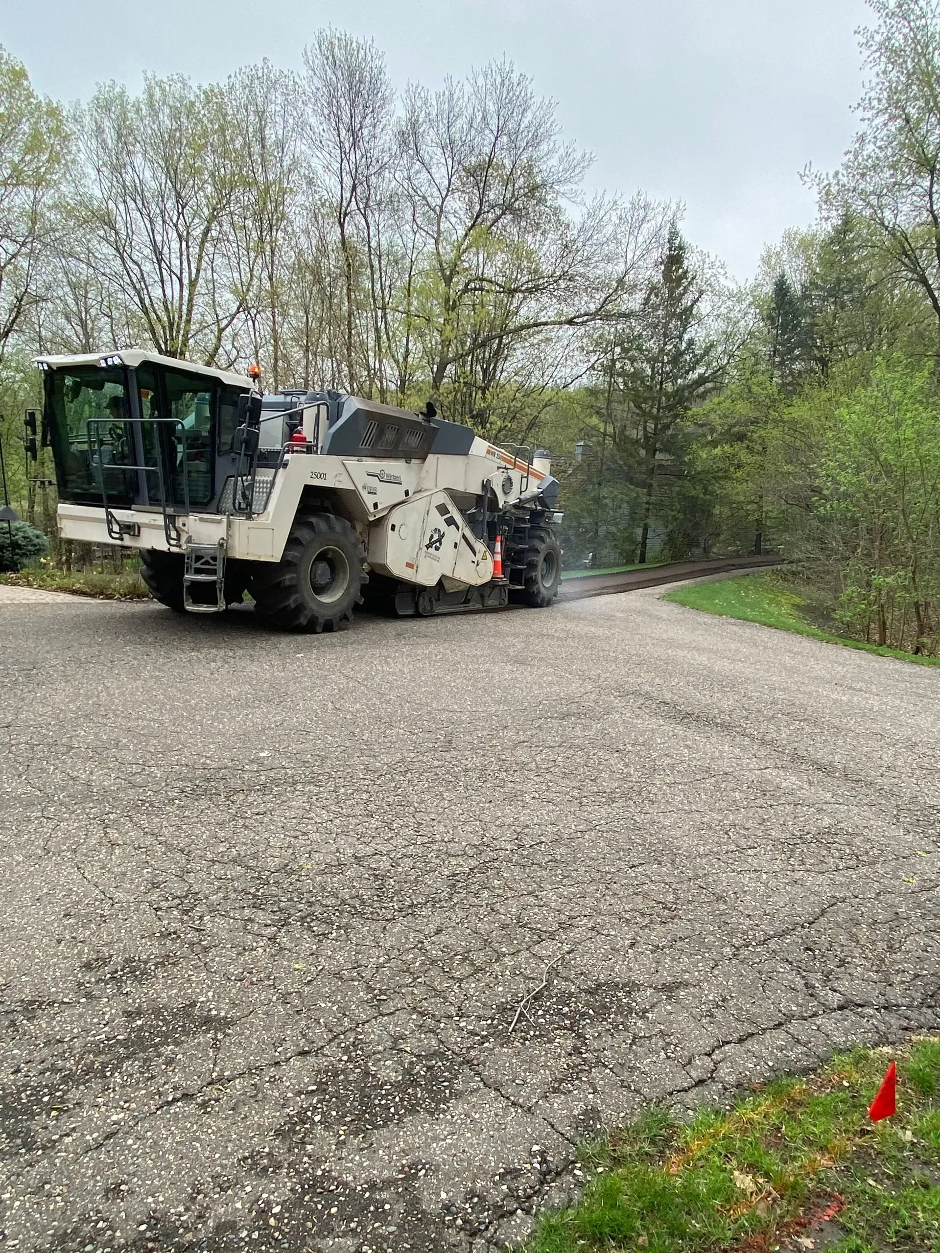 Road construction machine smoothing gravel on a road, trees in the background.