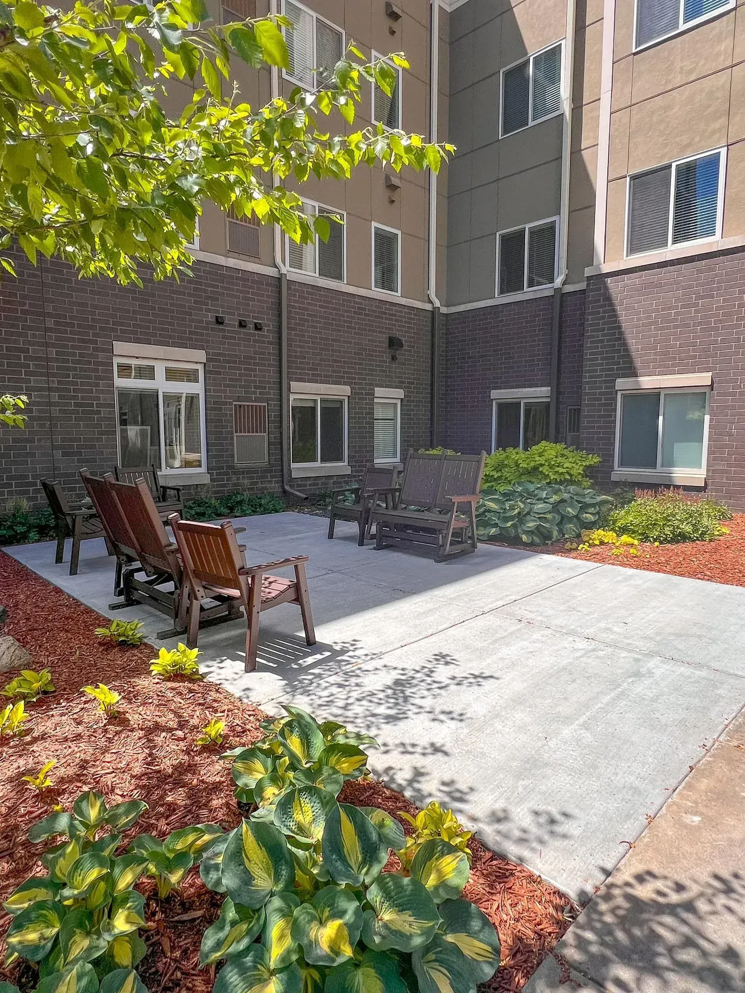 Outdoor courtyard with chairs, concrete patio, and landscaping against a multi-story building.