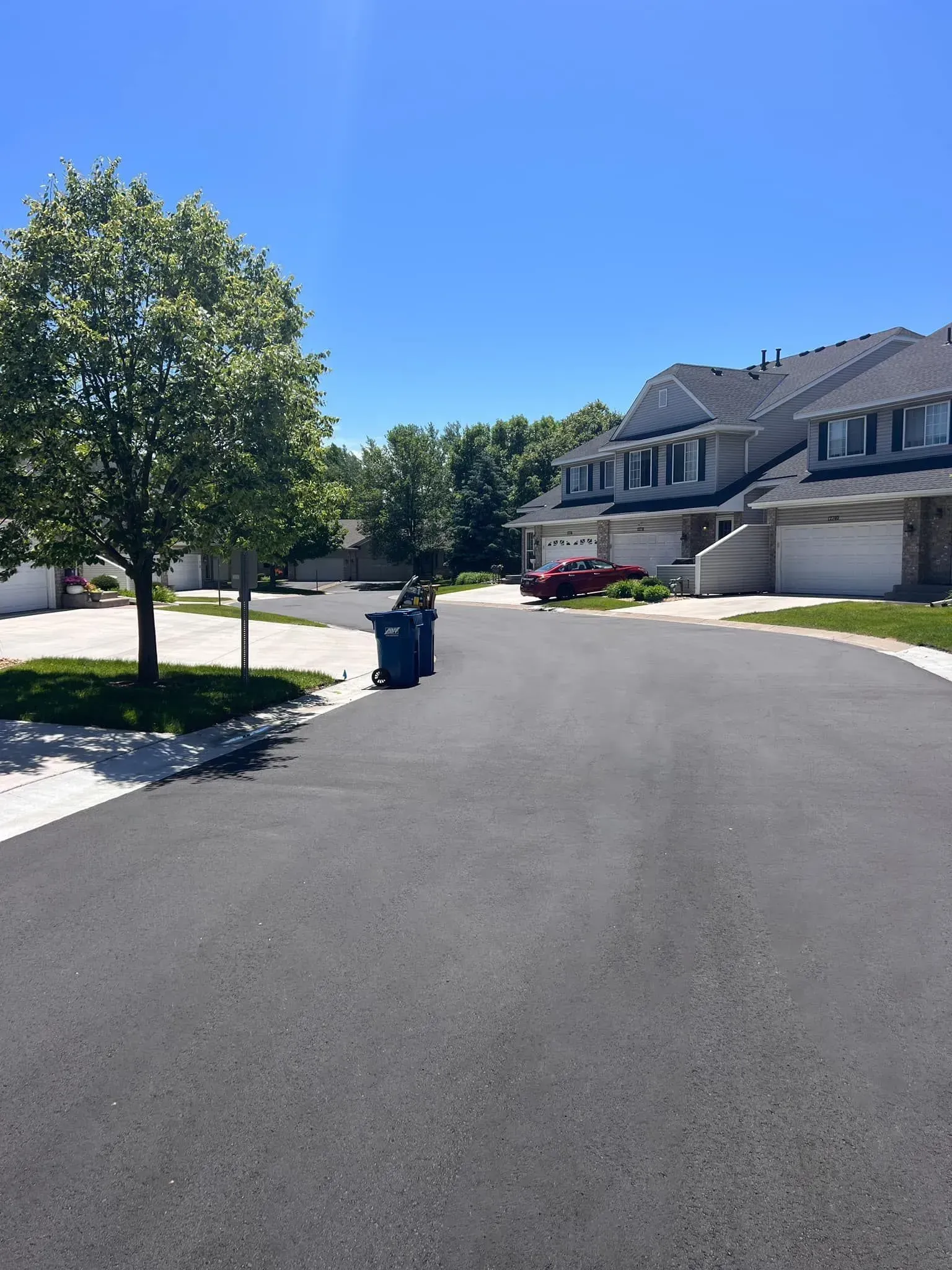 Asphalt road leading towards multi-unit housing with a blue sky and green trees.