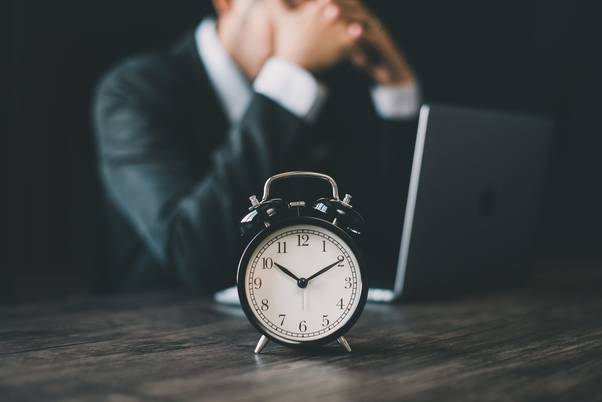 A man in a suit is sitting at a desk with an alarm clock in front of him. Running out of time.