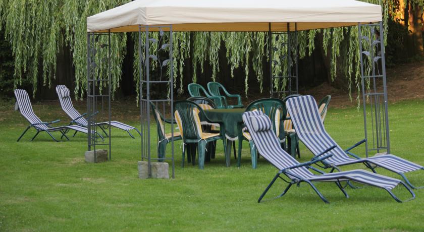 Auf einer Rasenfläche in der Nähe von Weiden steht eine Terrassengarnitur mit beigem Sonnensegel und Stühlen;
