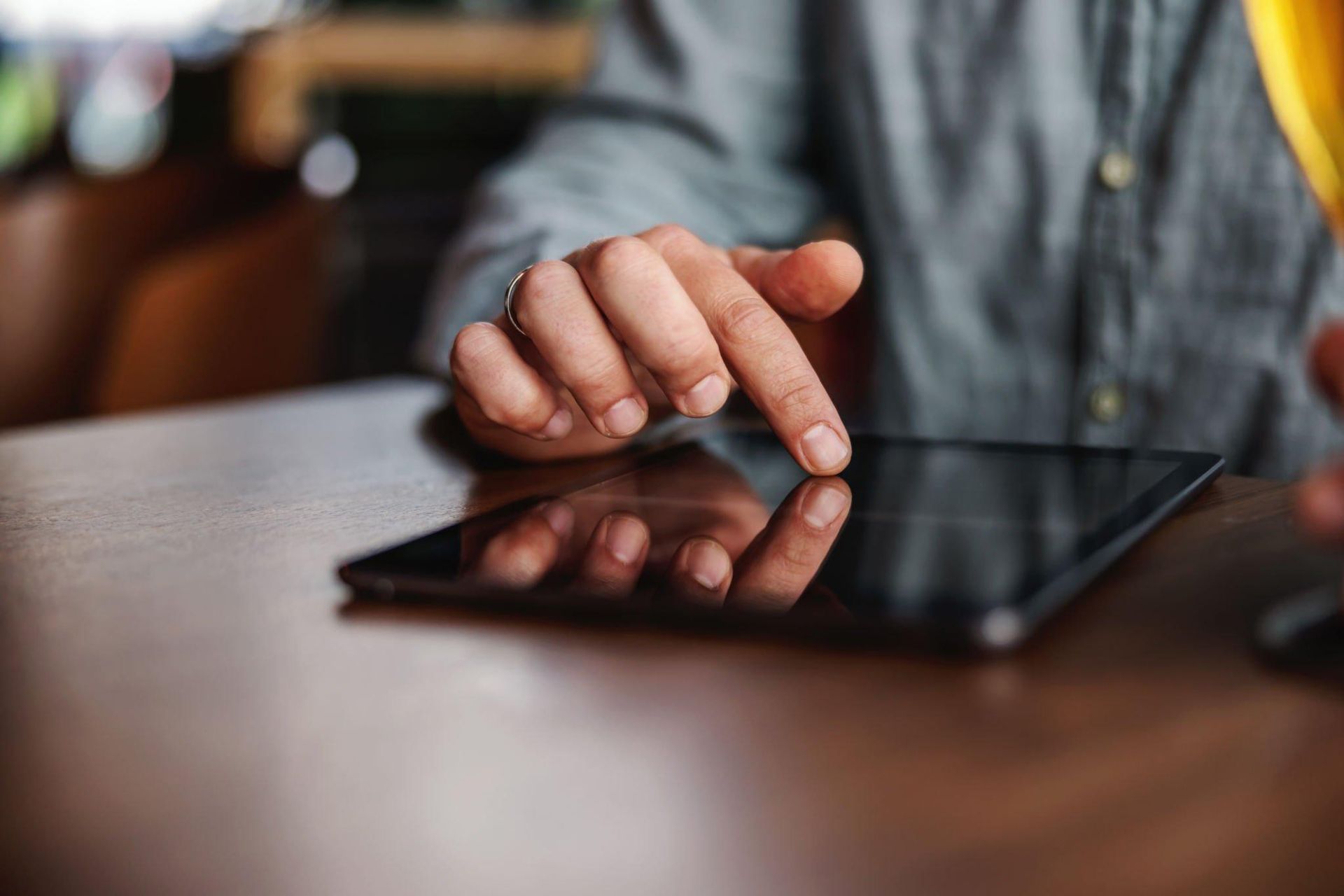 A person is using a tablet computer on a wooden table.