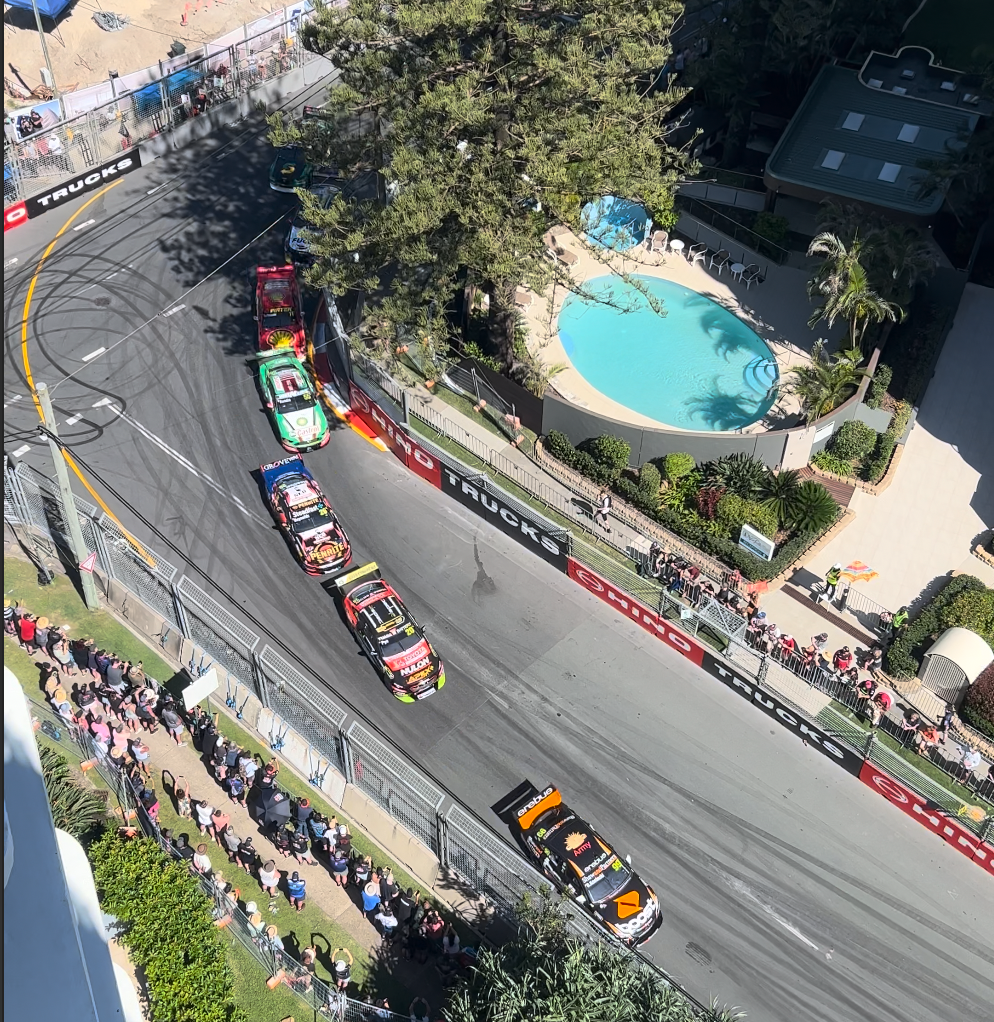 Gold Coast 500 race cars rounding a corner with spectators and apartment pool nearby.