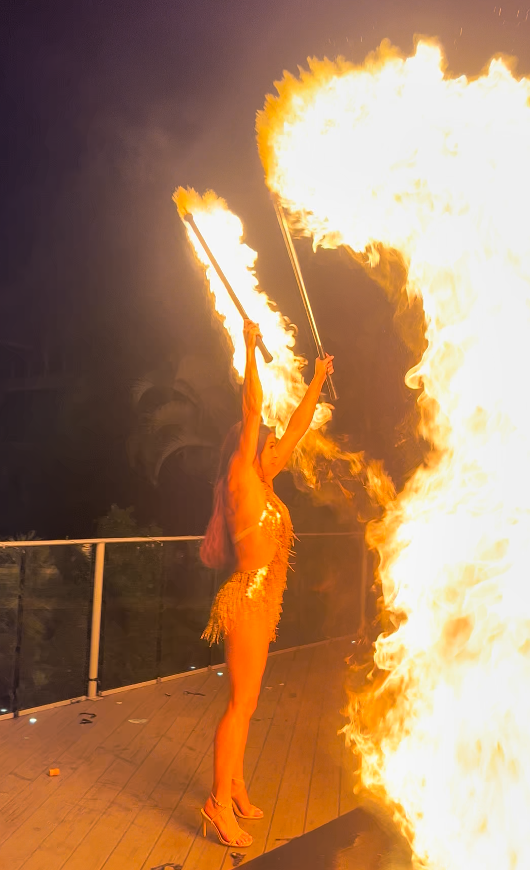 Woman in a shiny gold costume throwing a big fire performance.