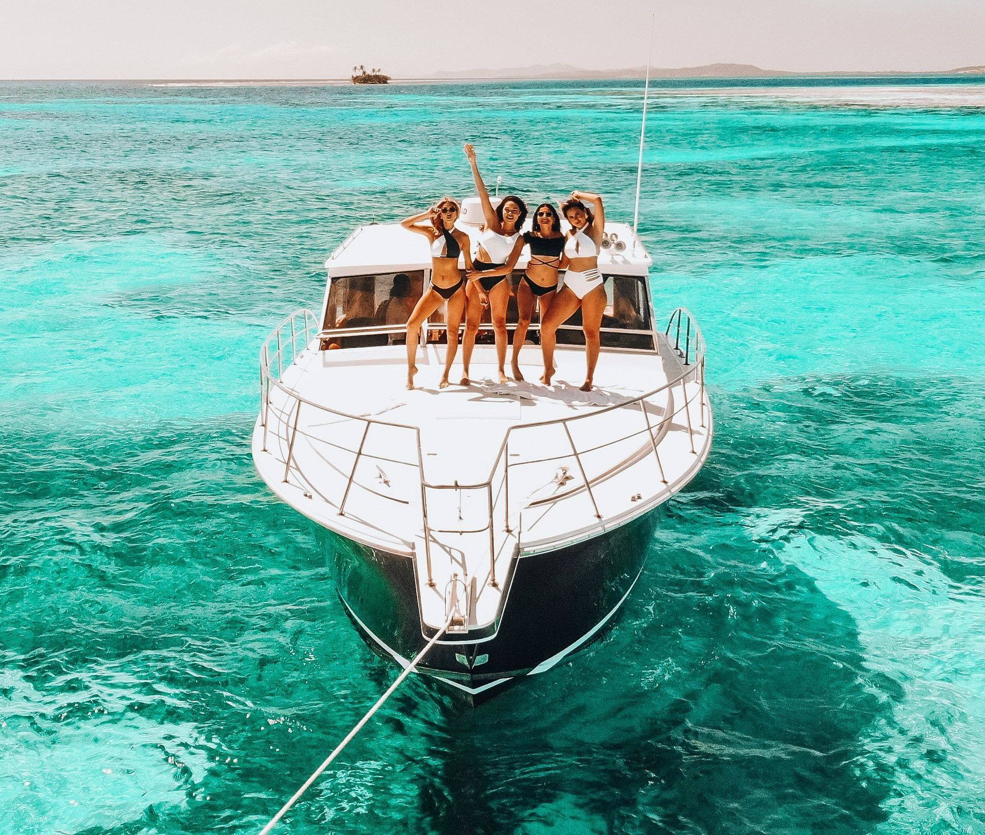 Women in bikinis celebrate on a yacht in crystal-clear water.