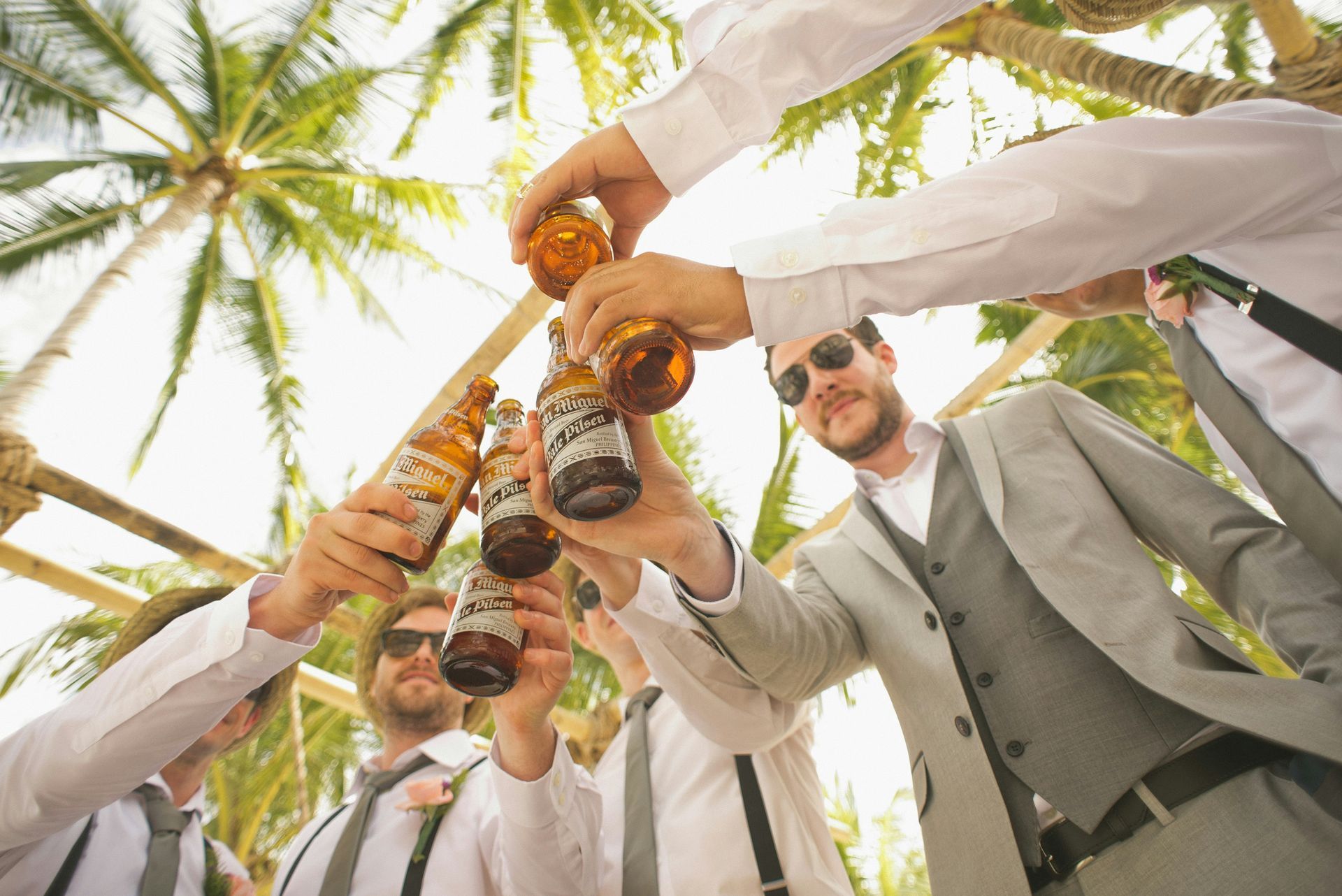 Stylish groomsmen toast cold beers at a tropical bucks party, capturing tropical vibes.