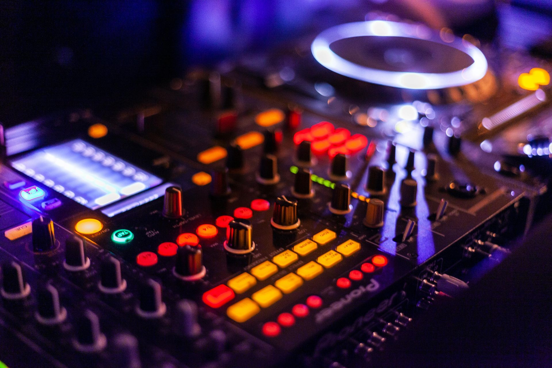 Close-up of illuminated Pioneer DJ mixer, colourful buttons and knobs glowing in moody club lighting.