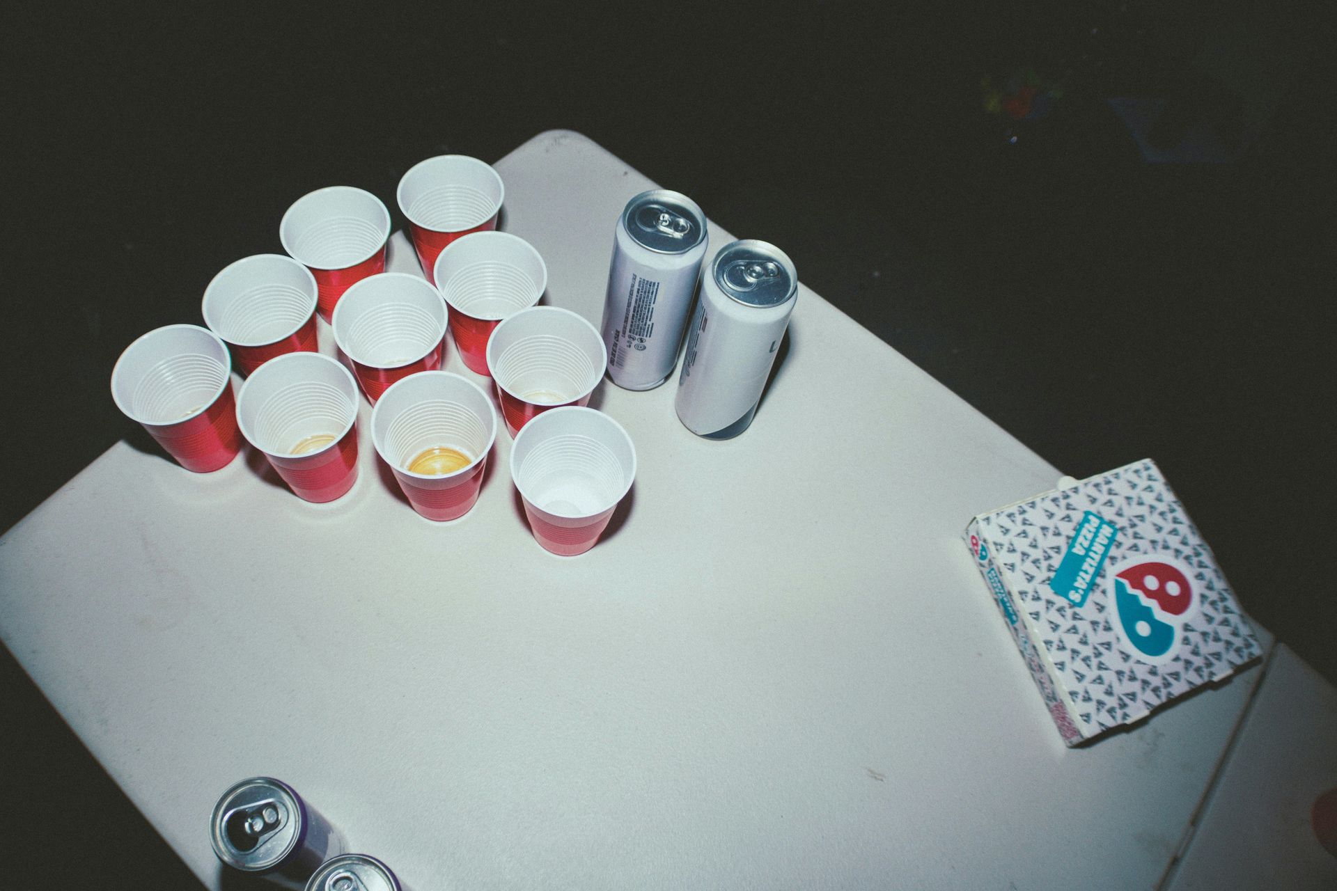 Red solo cups arranged for beer pong game with cans on white table.