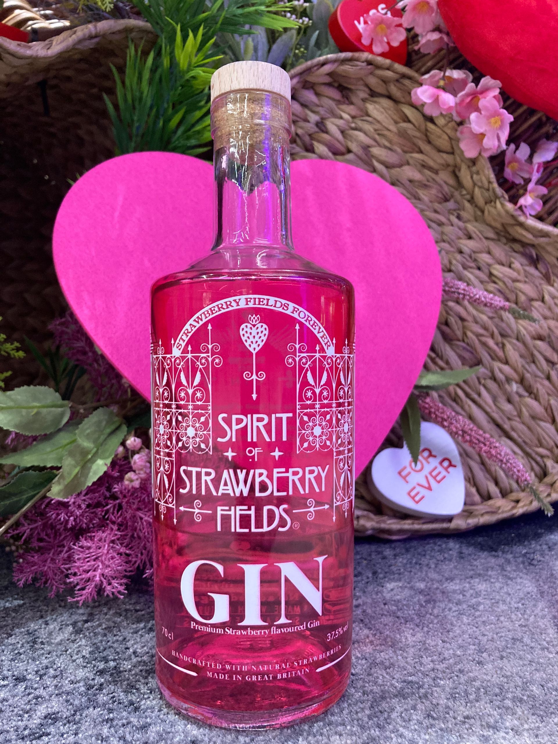 A bottle of strawberry Fields gin is sitting next to a pink heart which says forever