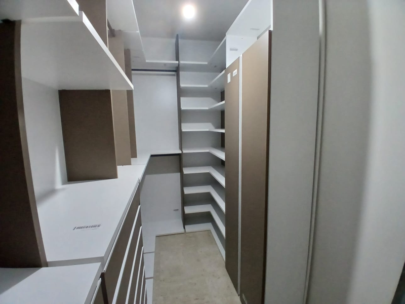 Cabina armadio vuota e organizzata con ripiani bianchi e marroni. Corridoio centrale con ripiani su entrambi i lati, ben illuminato.