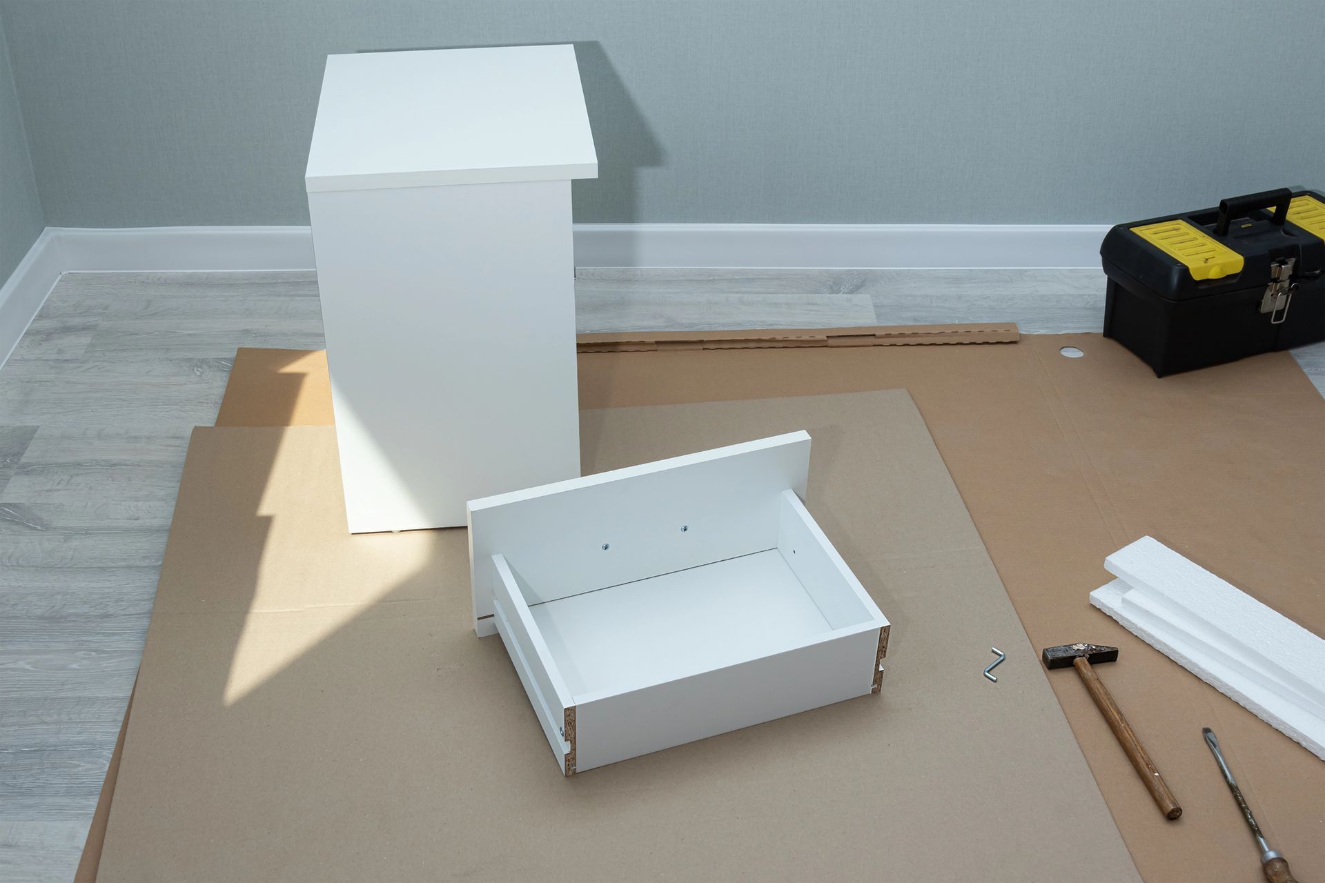 Componenti bianchi del mobile e cassetto disposti per il montaggio, con attrezzi su cartone.
