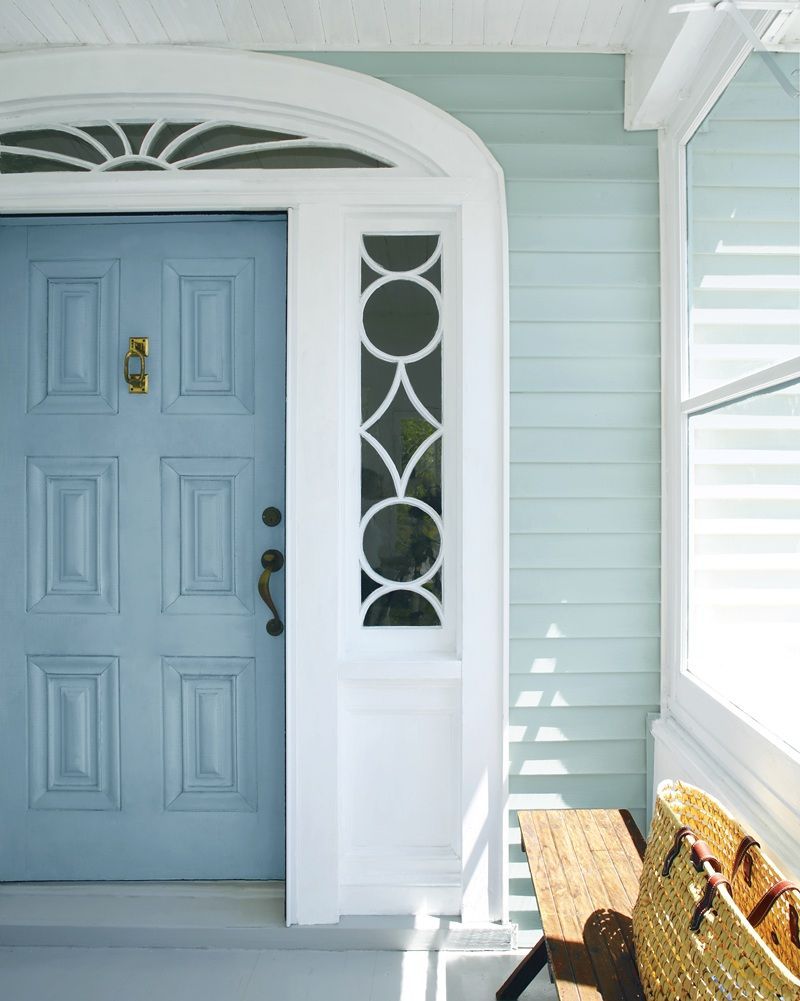 Blue front door with white trim and sidelights beside a porch bench in a light blue house exterior