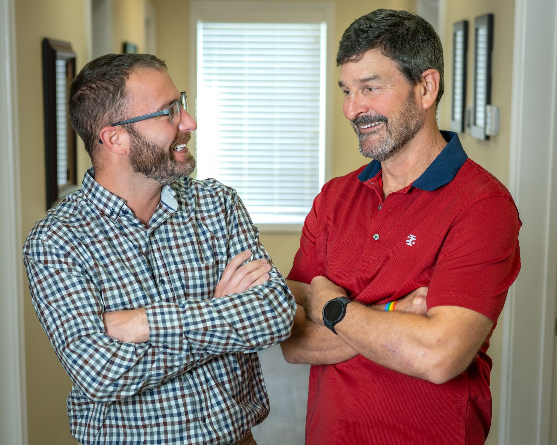 Two men are standing next to each other in a hallway with their arms crossed.