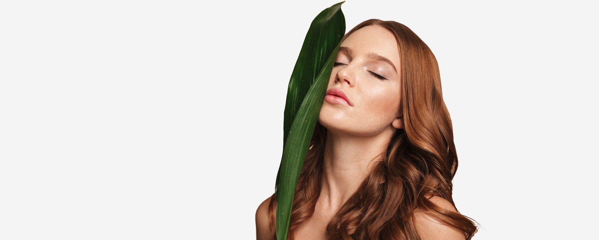 A woman is holding a green leaf in front of her face.
