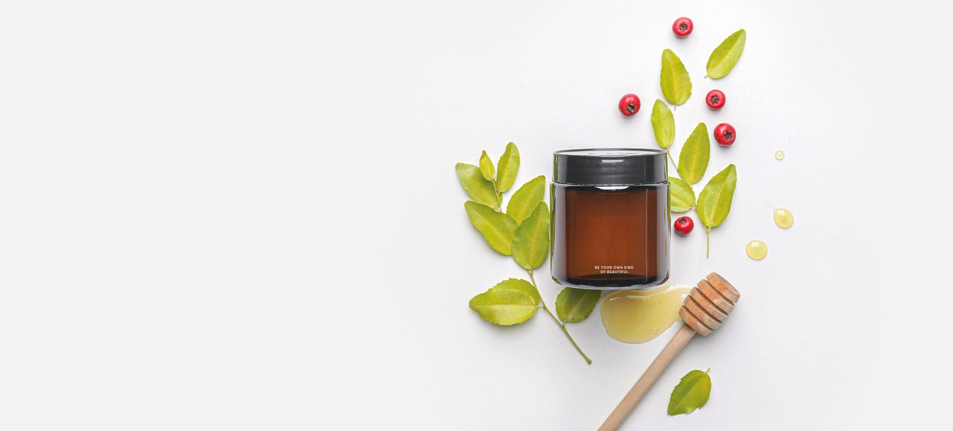 A jar of honey surrounded by leaves and berries on a white background.