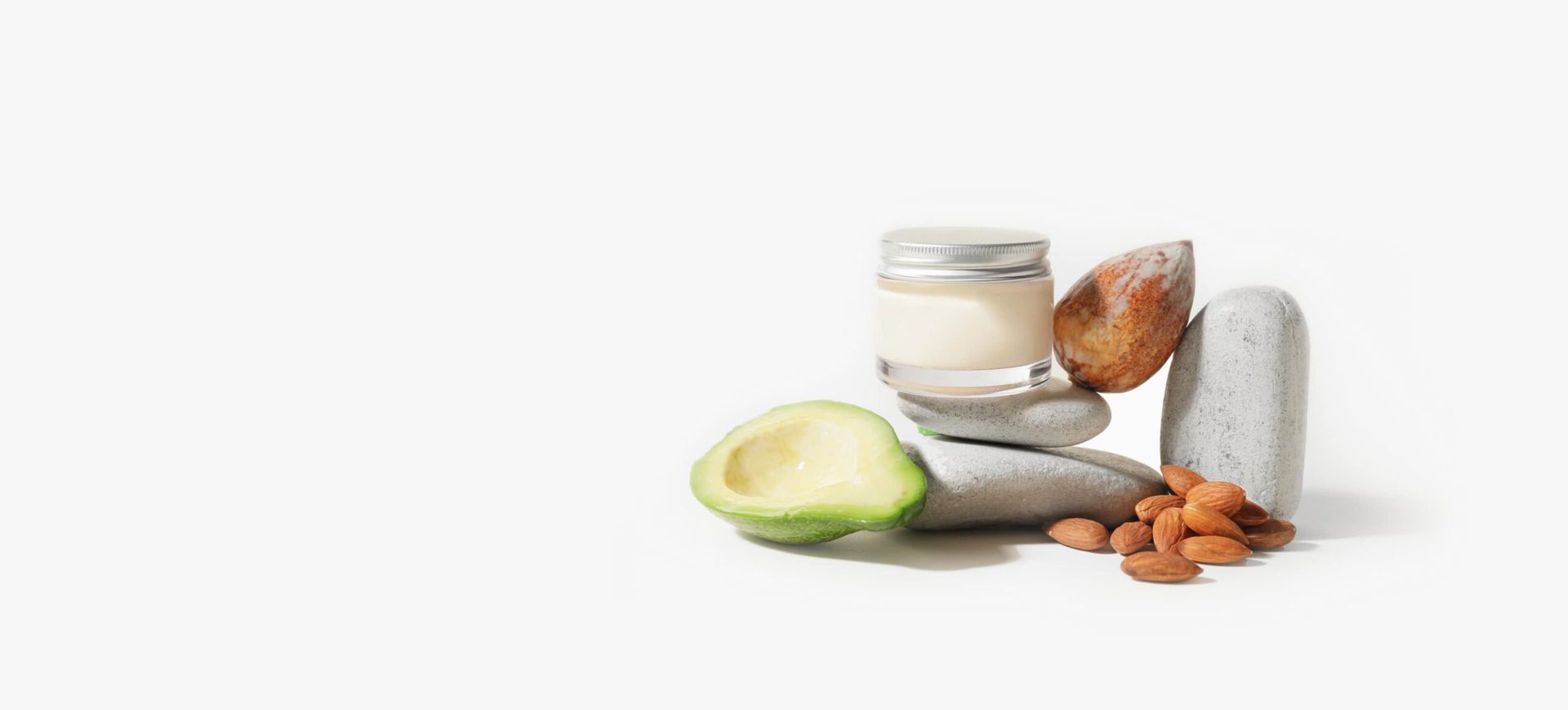 A jar of yogurt, avocado, almonds and rocks on a white background.