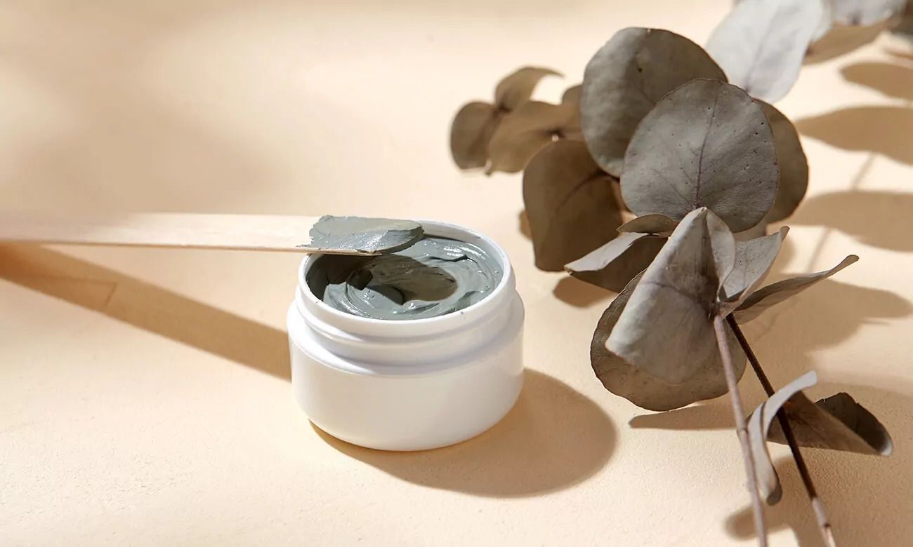 A jar of clay next to a plant with leaves on a table.