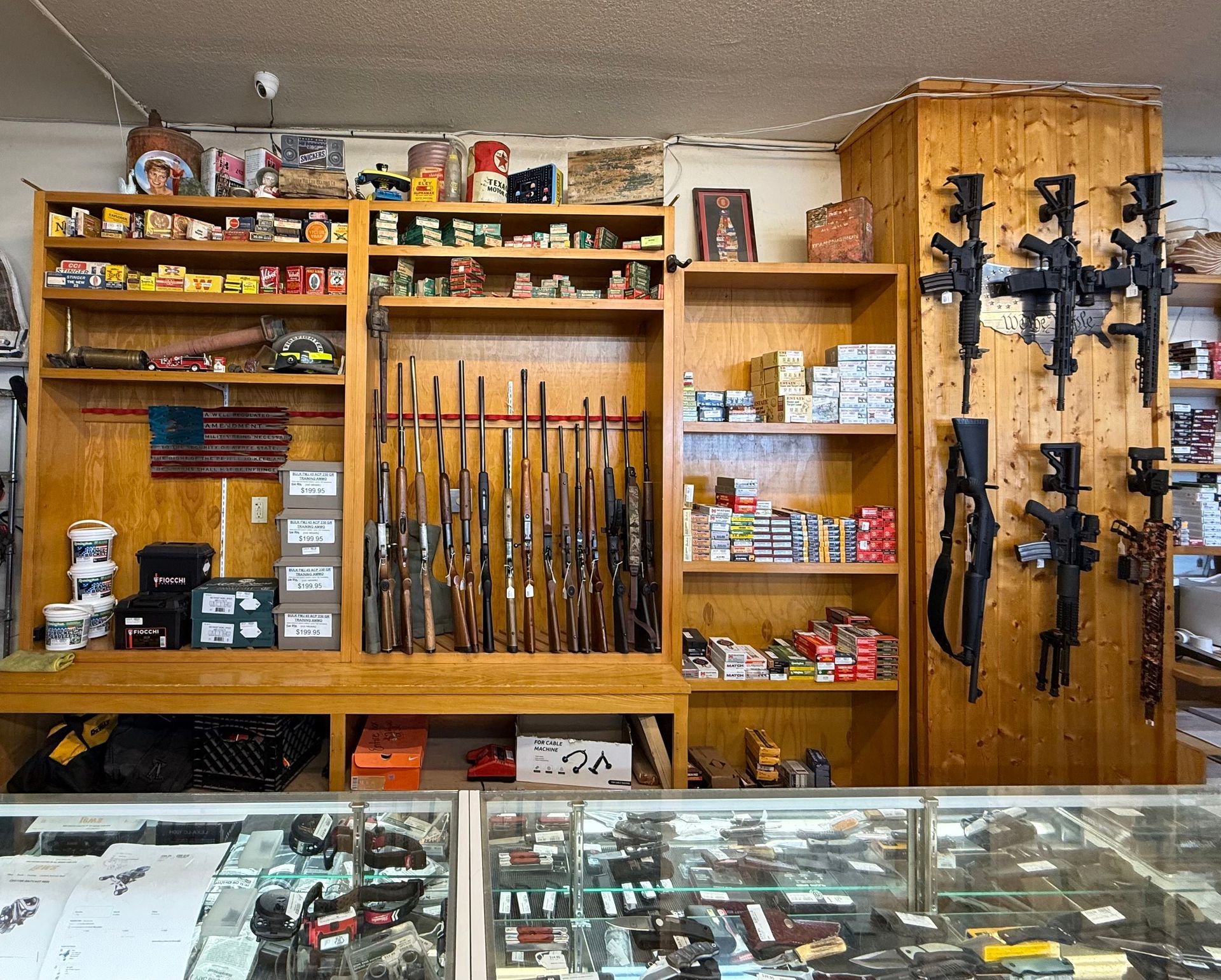 Inside a gun store, firearms and ammunition displayed on shelves and hanging on walls.