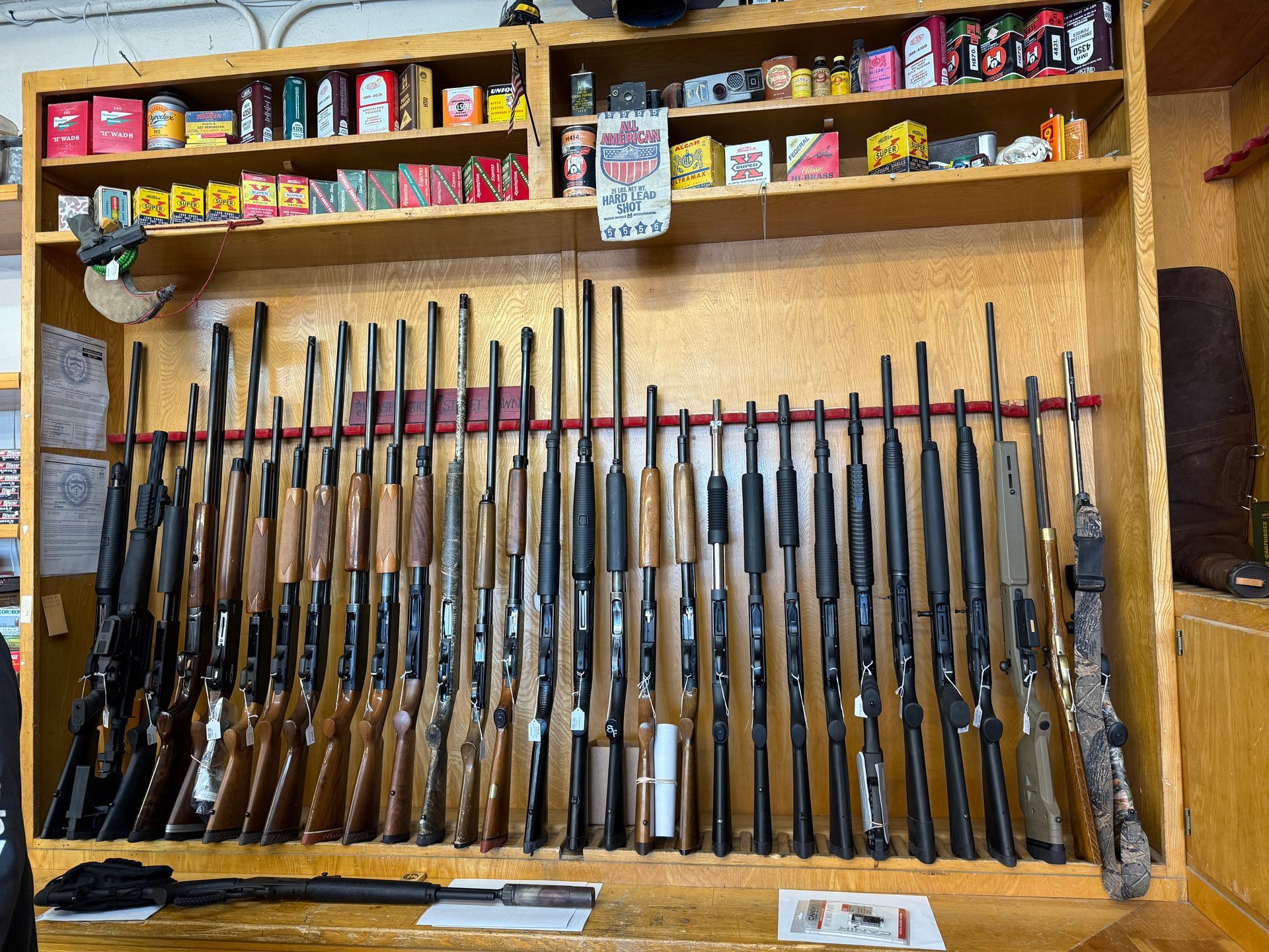 Guns displayed on a wooden shelf in a shop, with ammunition above.
