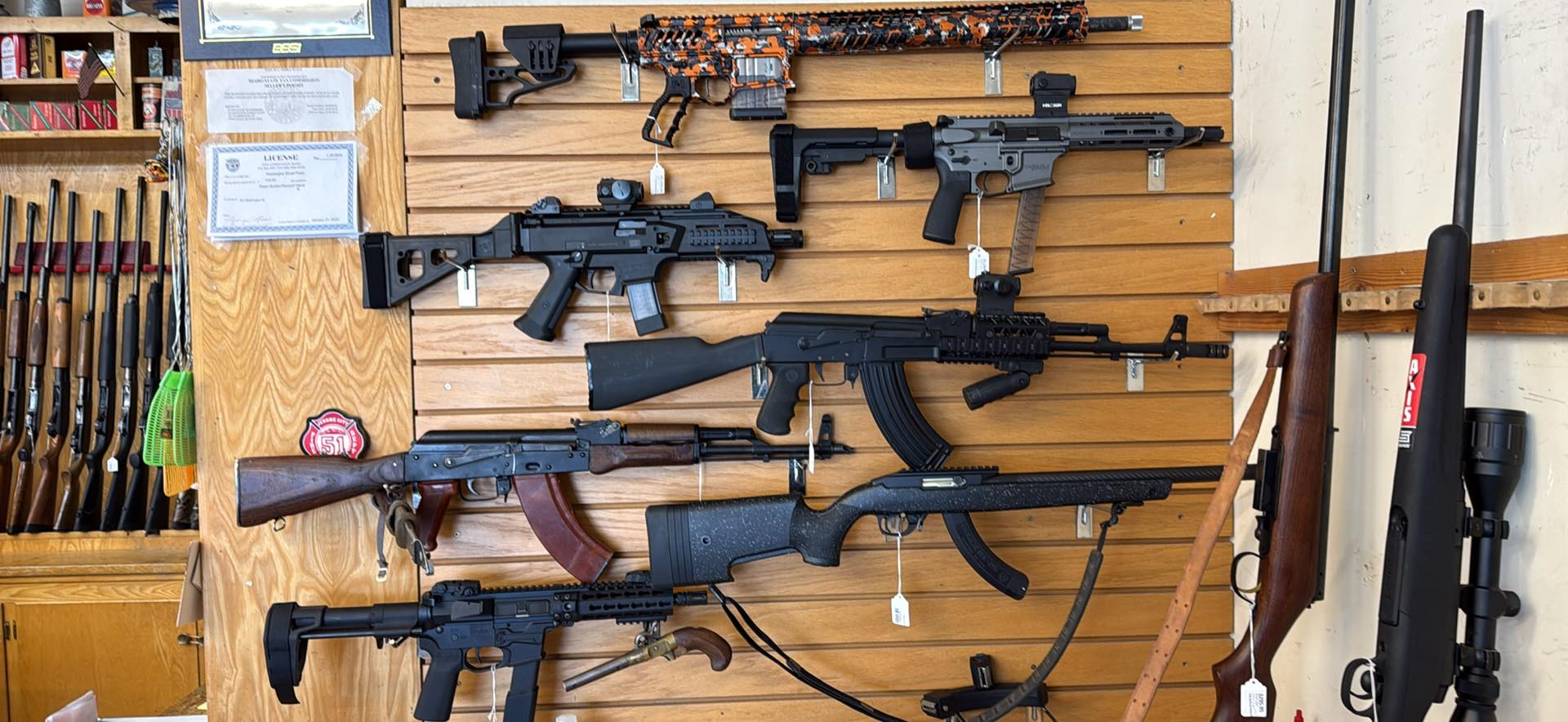 Guns on display at a gun store, including rifles and shotguns, mounted on a wooden wall.