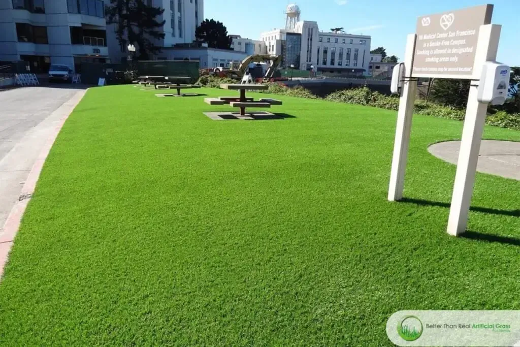 Green lawn with picnic tables and a sign, a building in the background.