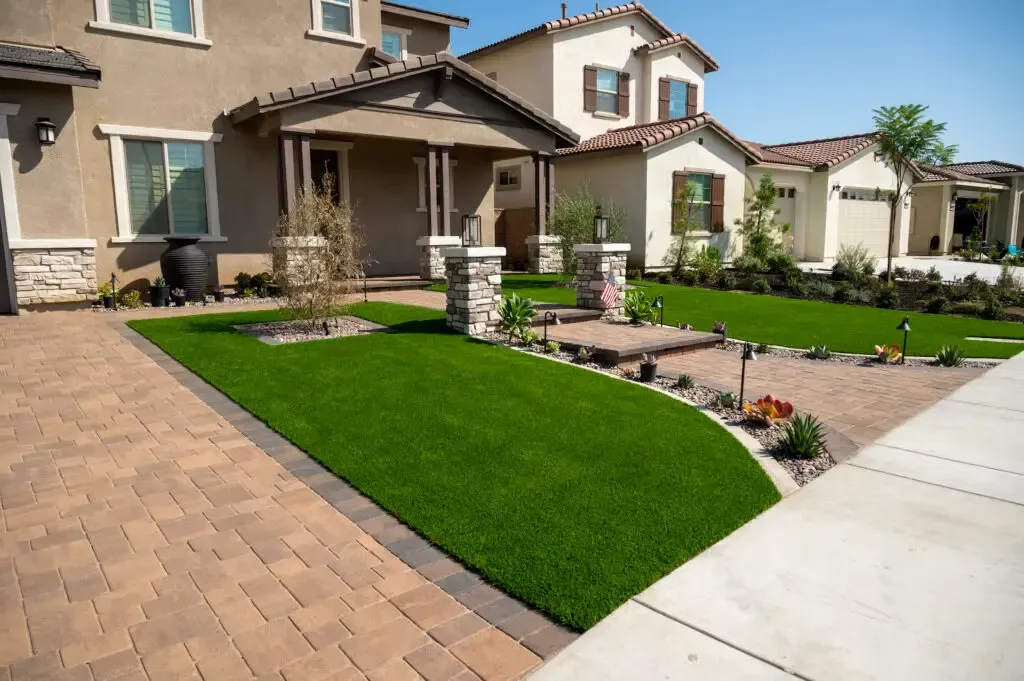 Residential home with lush green lawn, brick driveway, and stone accents.