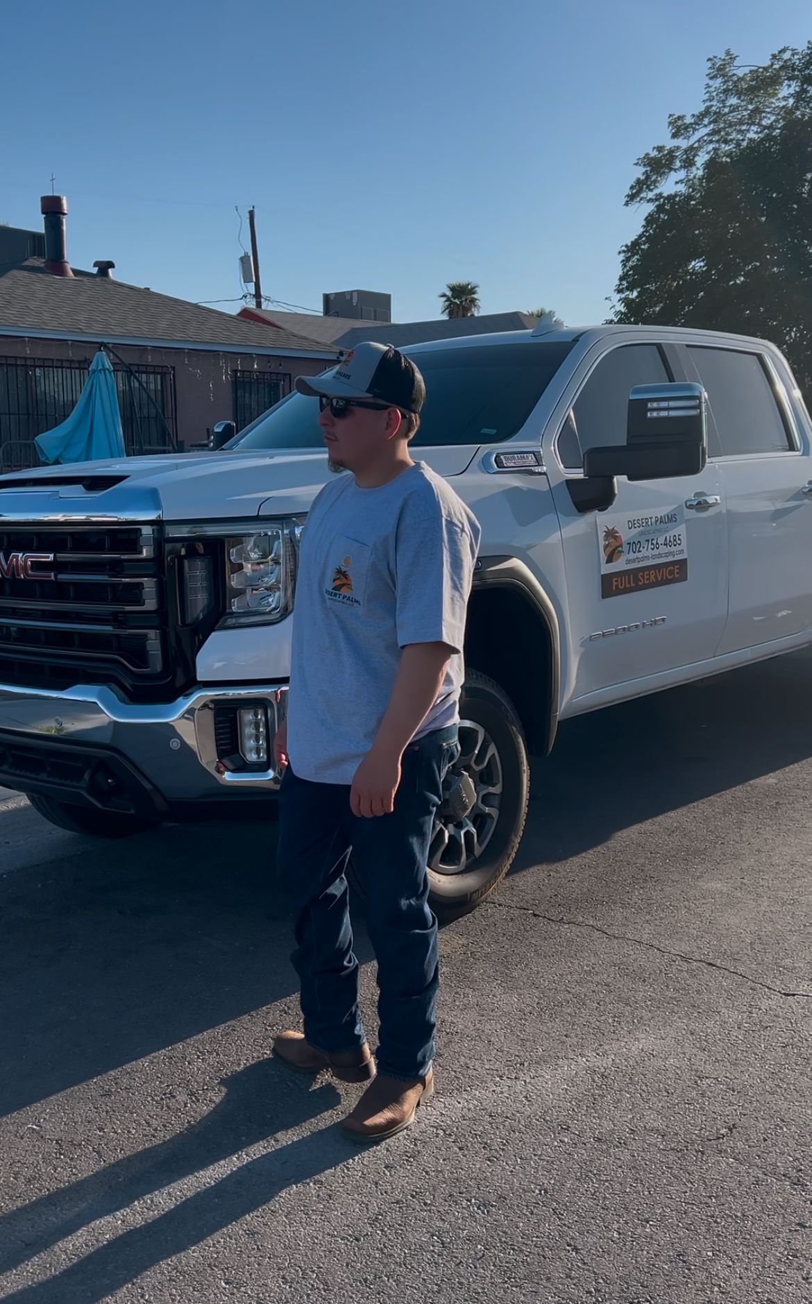Man in work clothes stands by white GMC truck. Sunny outdoor setting.