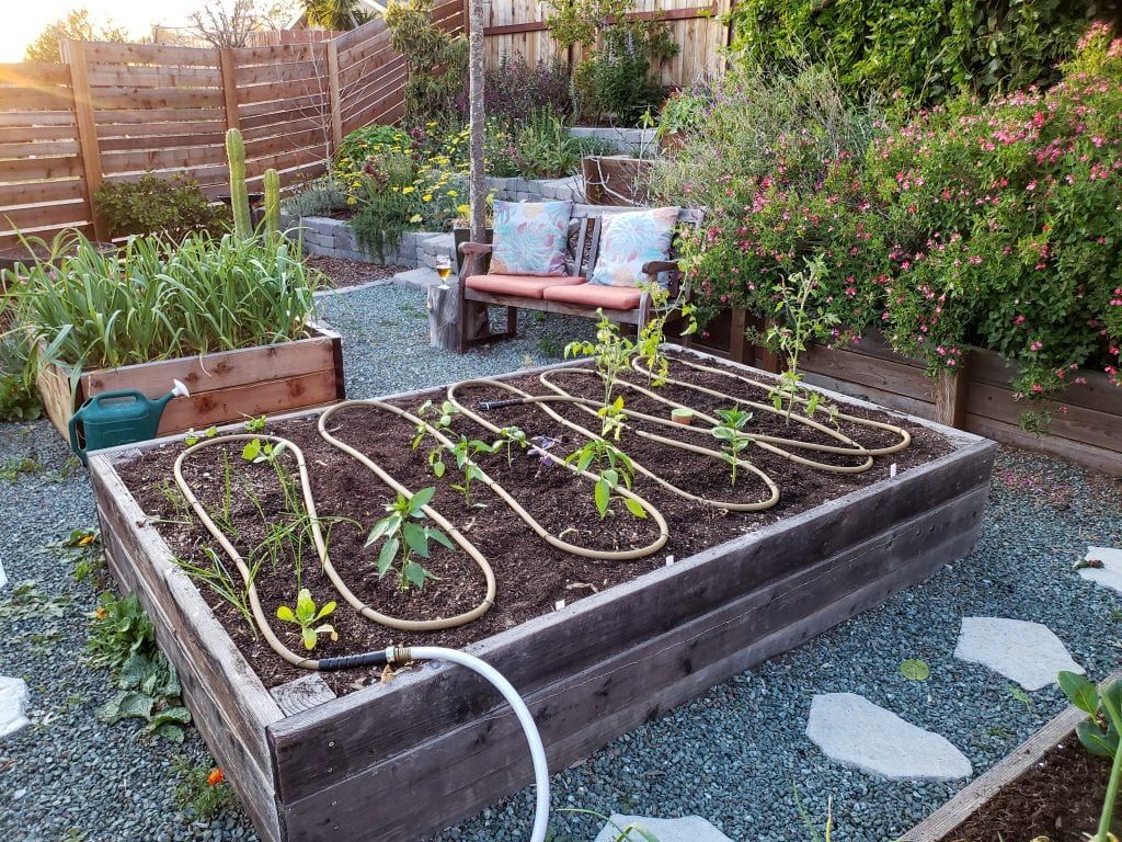 Raised garden bed with irrigation, plants, and a small seating area.