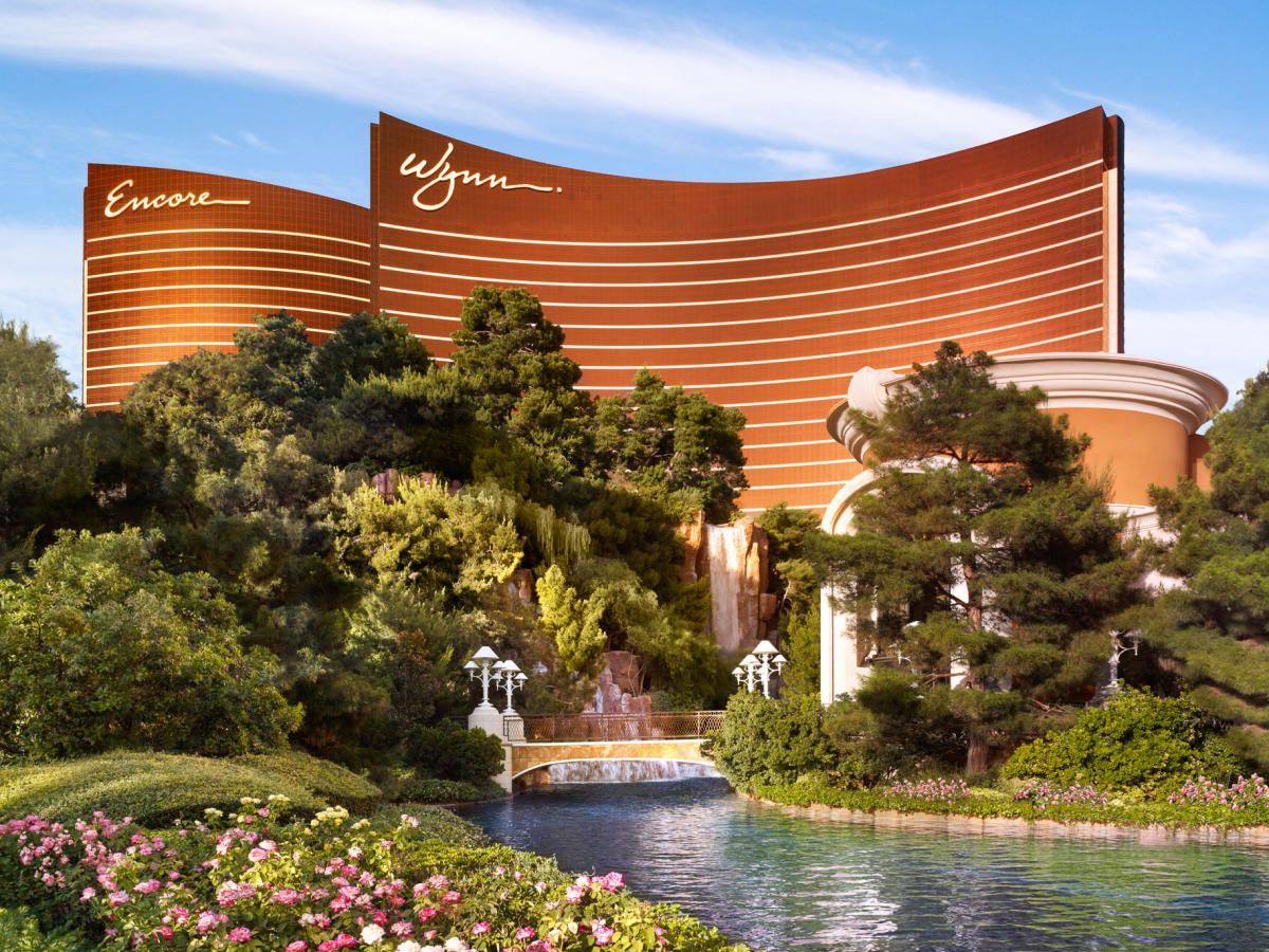 Wynn and Encore Las Vegas hotel complex with copper-colored towers and lush greenery, including a pond and waterfall.