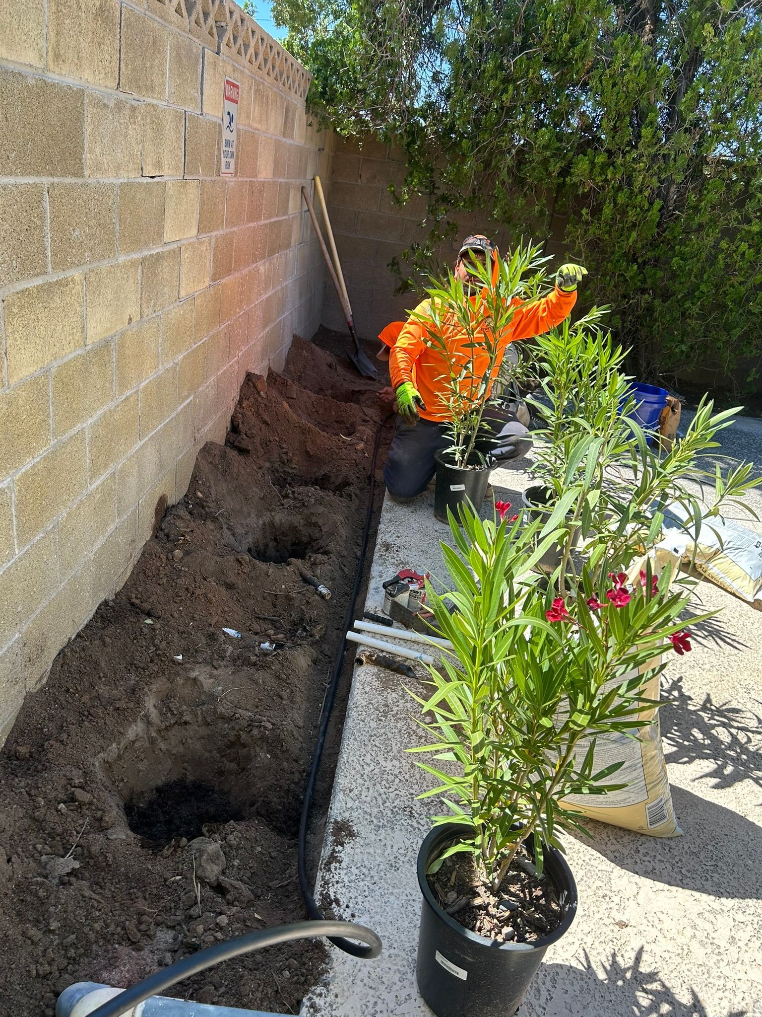 A prepared garden bed along a brick wall, with potted plants and tools ready for planting.