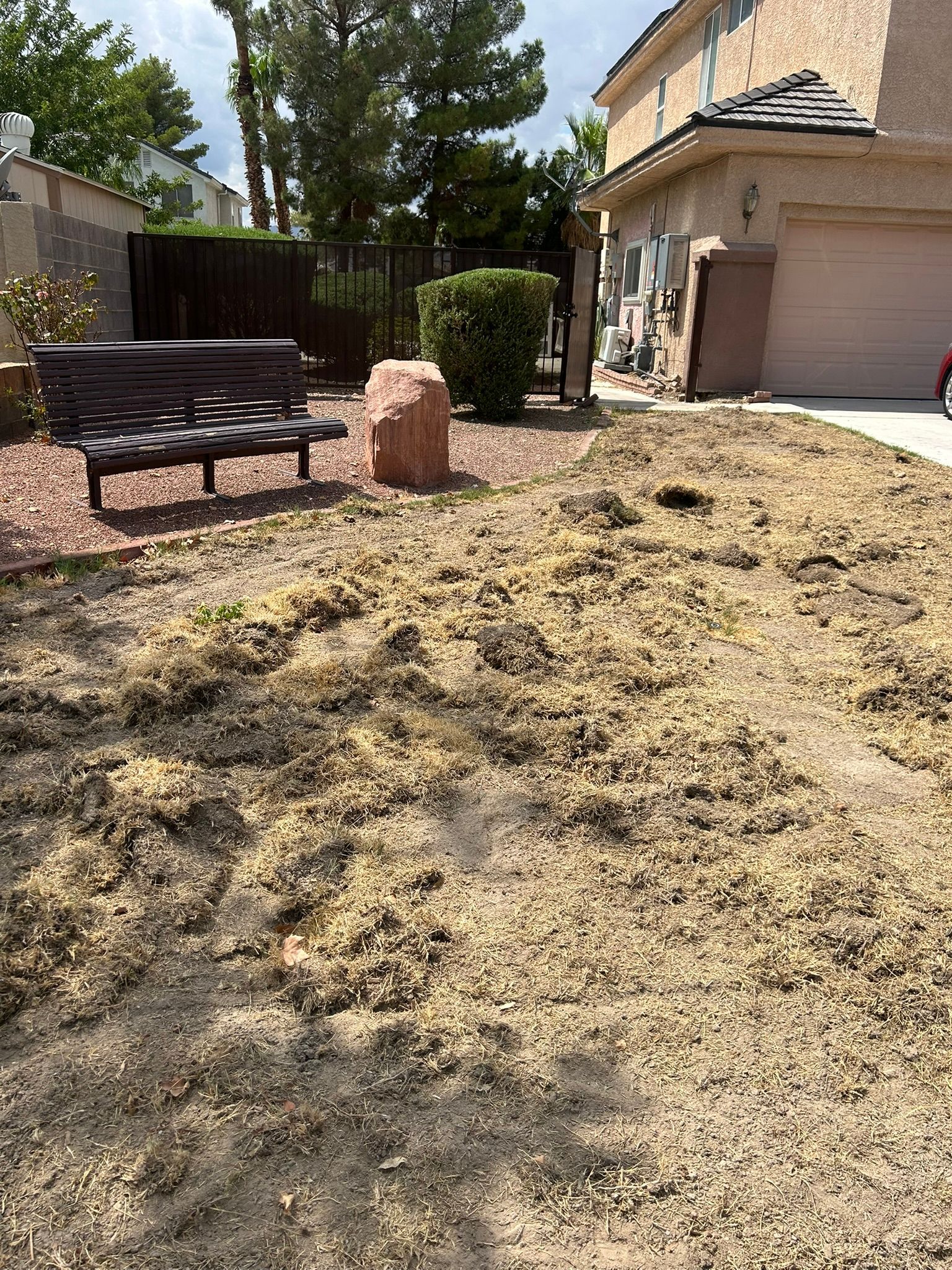 Yard with dead grass, a bench, rock, and house in the background.