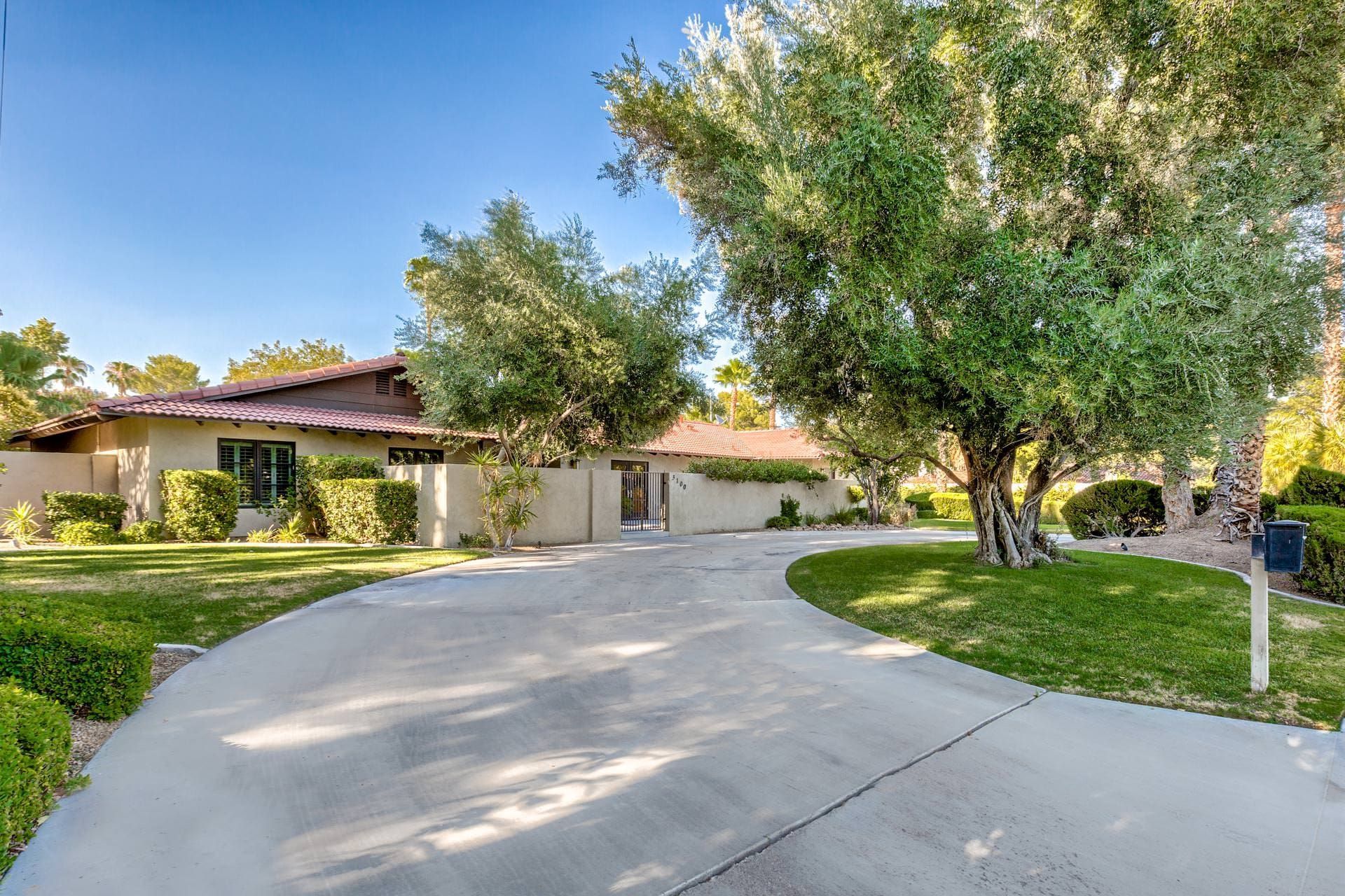 A beige stucco house with a curved driveway and lush greenery.
