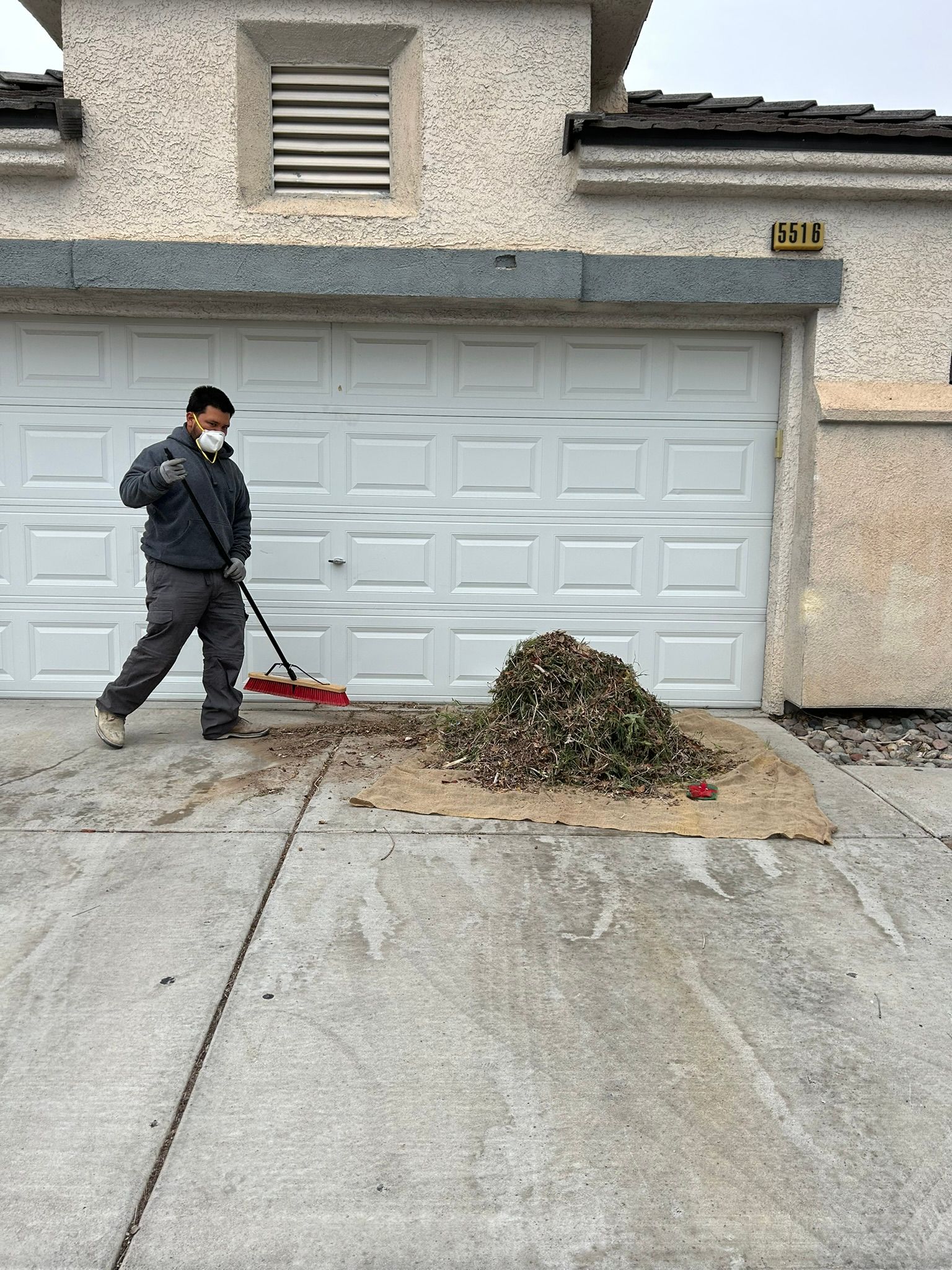 Man in mask sweeping leaves in front of a garage door.