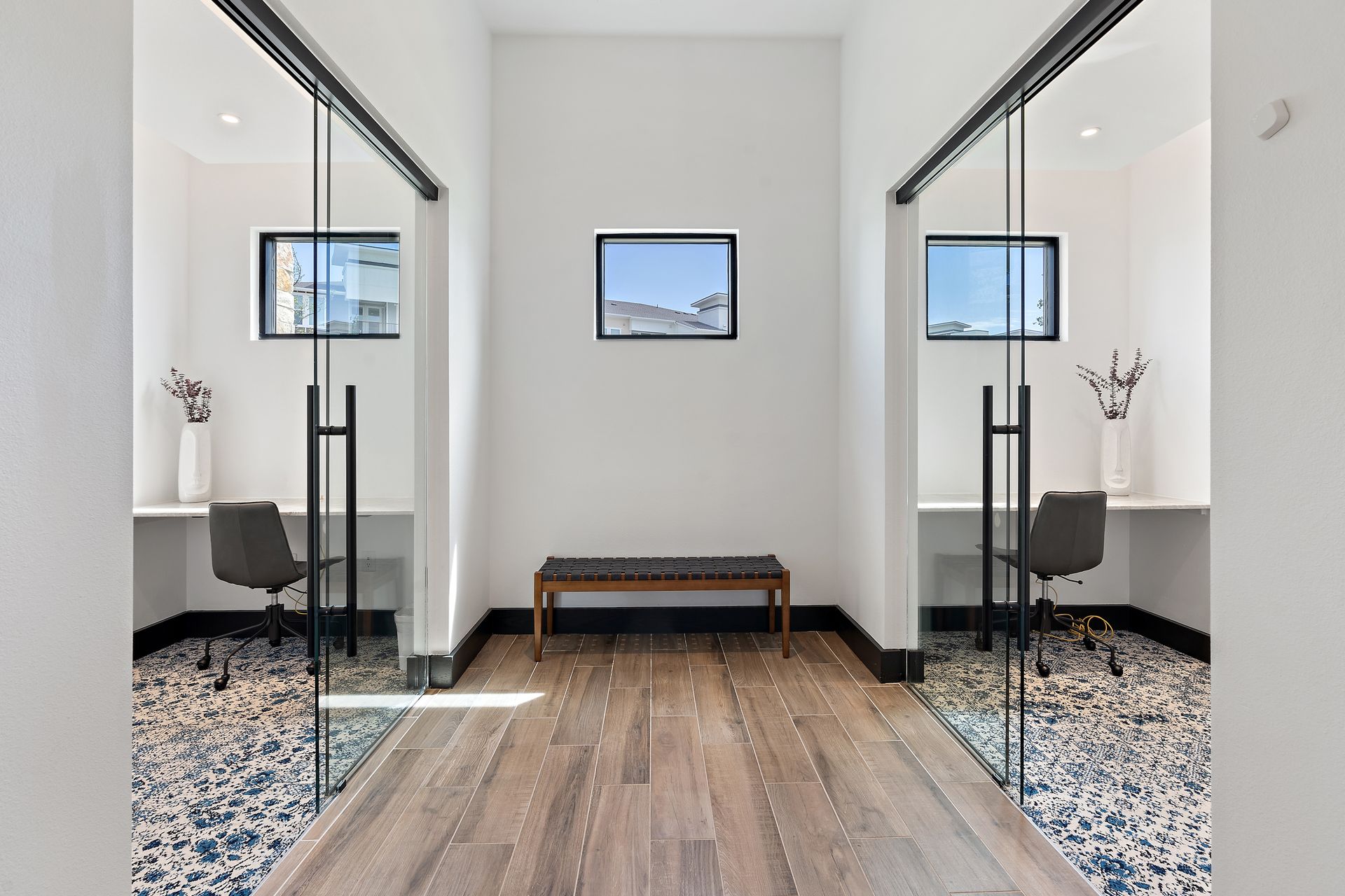 Symmetrical hallway with two glass-walled offices and a bench in the center.