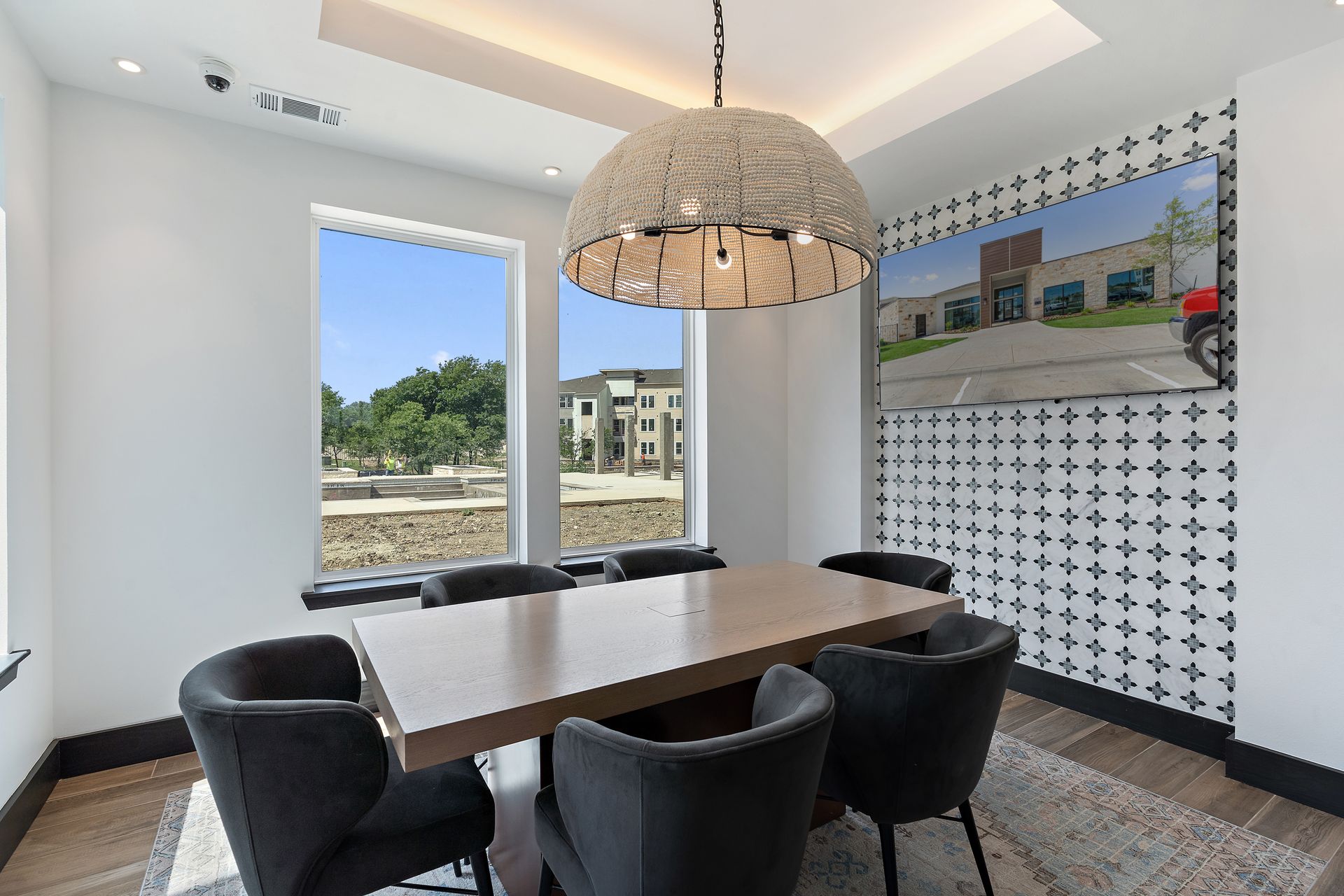 Modern community dining area with a long table, six chairs, pendant light, and wall TV.