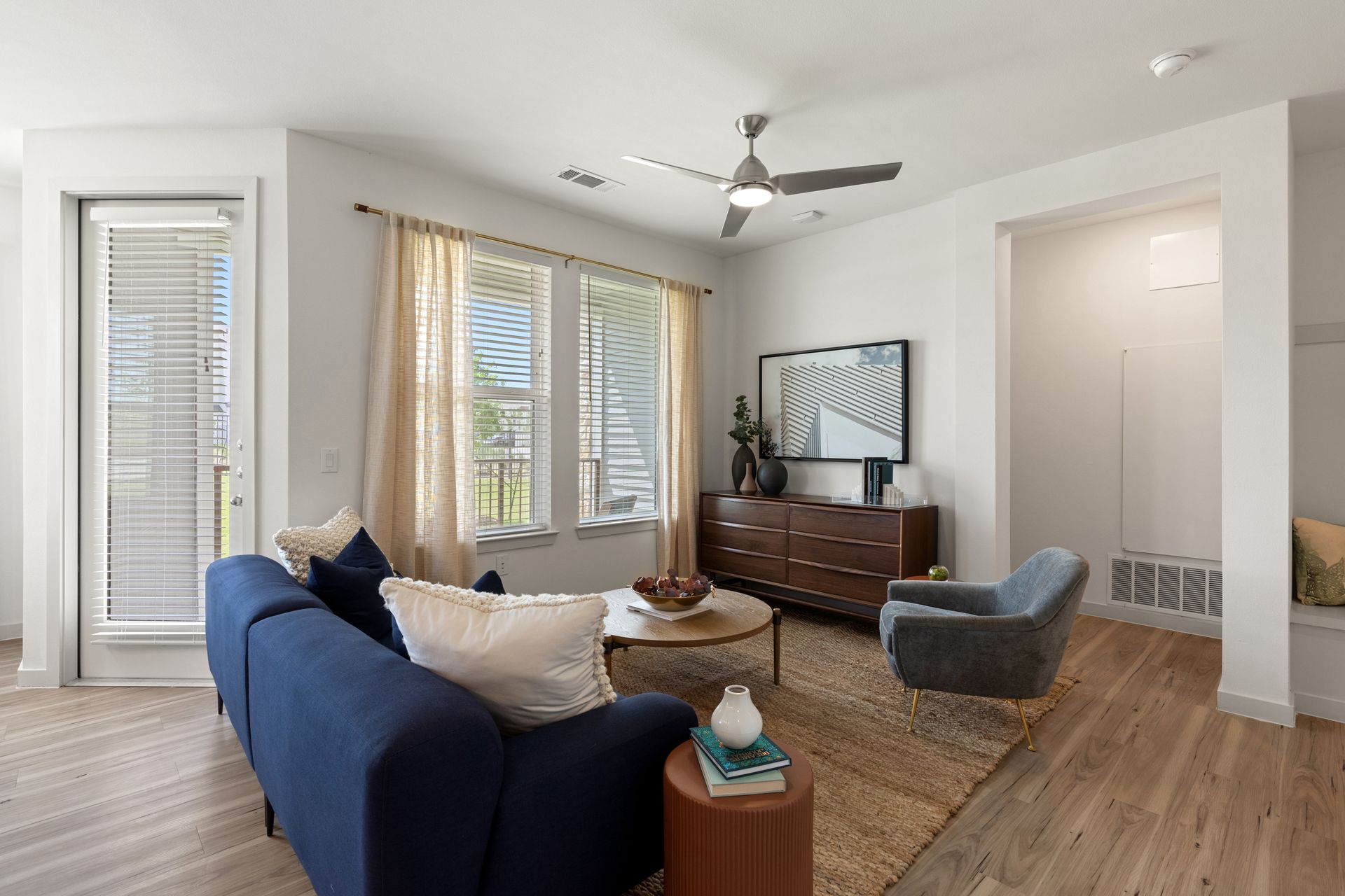 Bright living room with a blue sofa, beige curtains, large windows, and a mid-century dresser.
