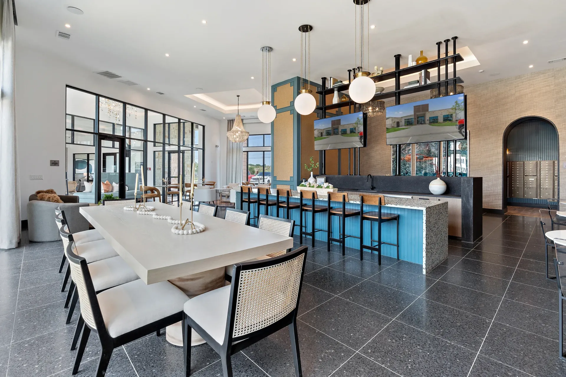 Bright contemporary community lounge with a long white dining table, blue bar, and hanging globe lights.