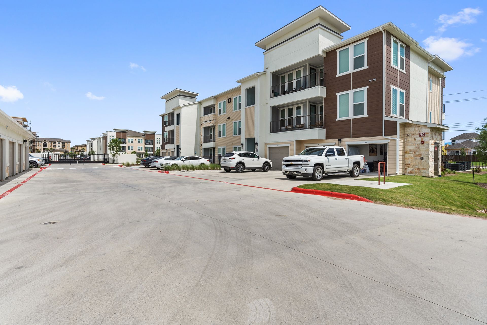 Exterior view of modern apartment buildings with a paved parking lot and garages.