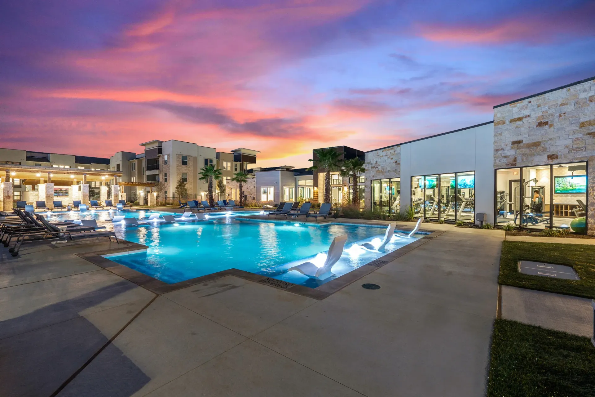 Outdoor resort-style pool with lounge chairs at a modern apartment community at sunset.
