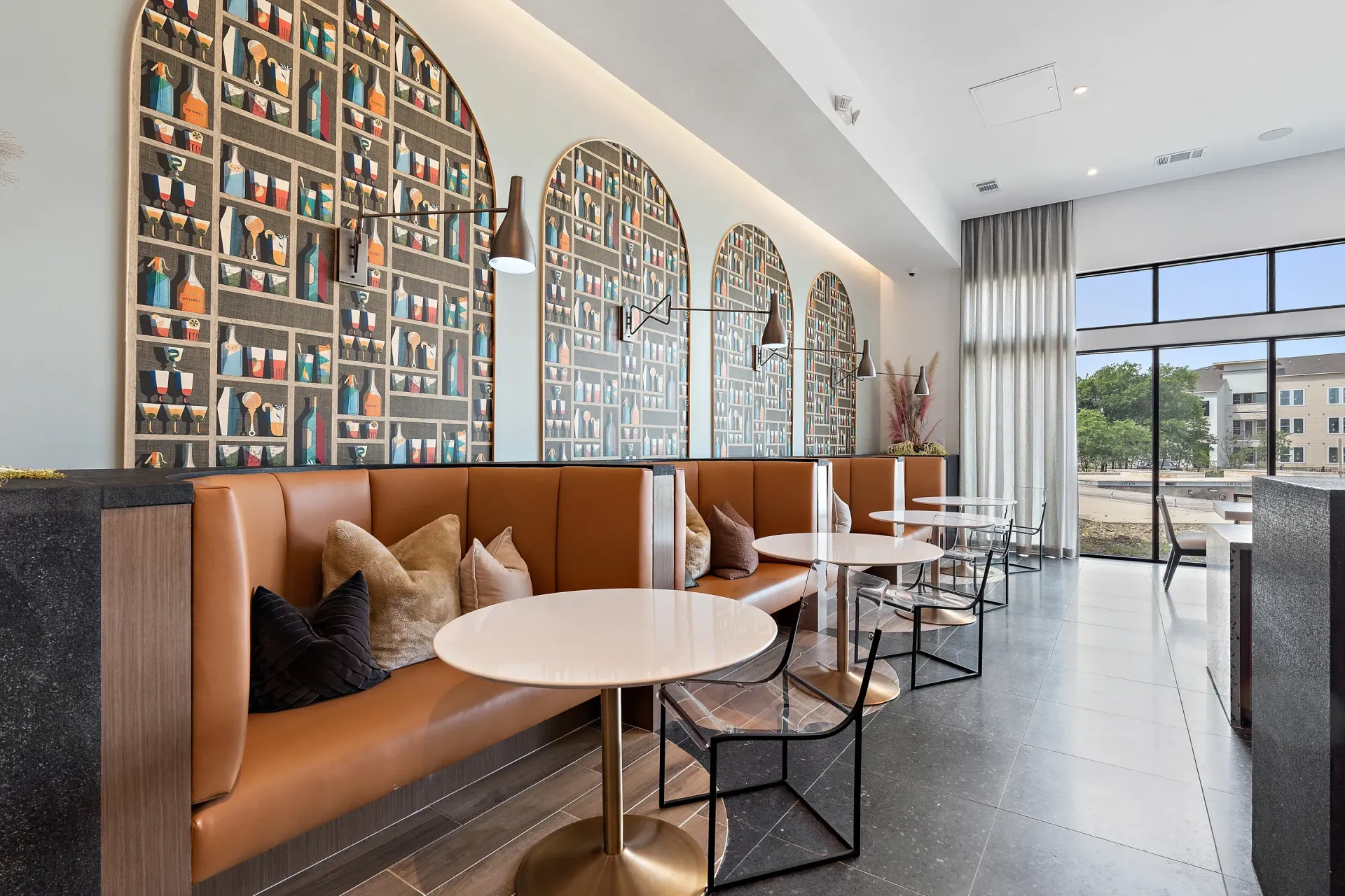 Modern apartment community lounge with tan leather booths, round white tables, wall art, and large windows.